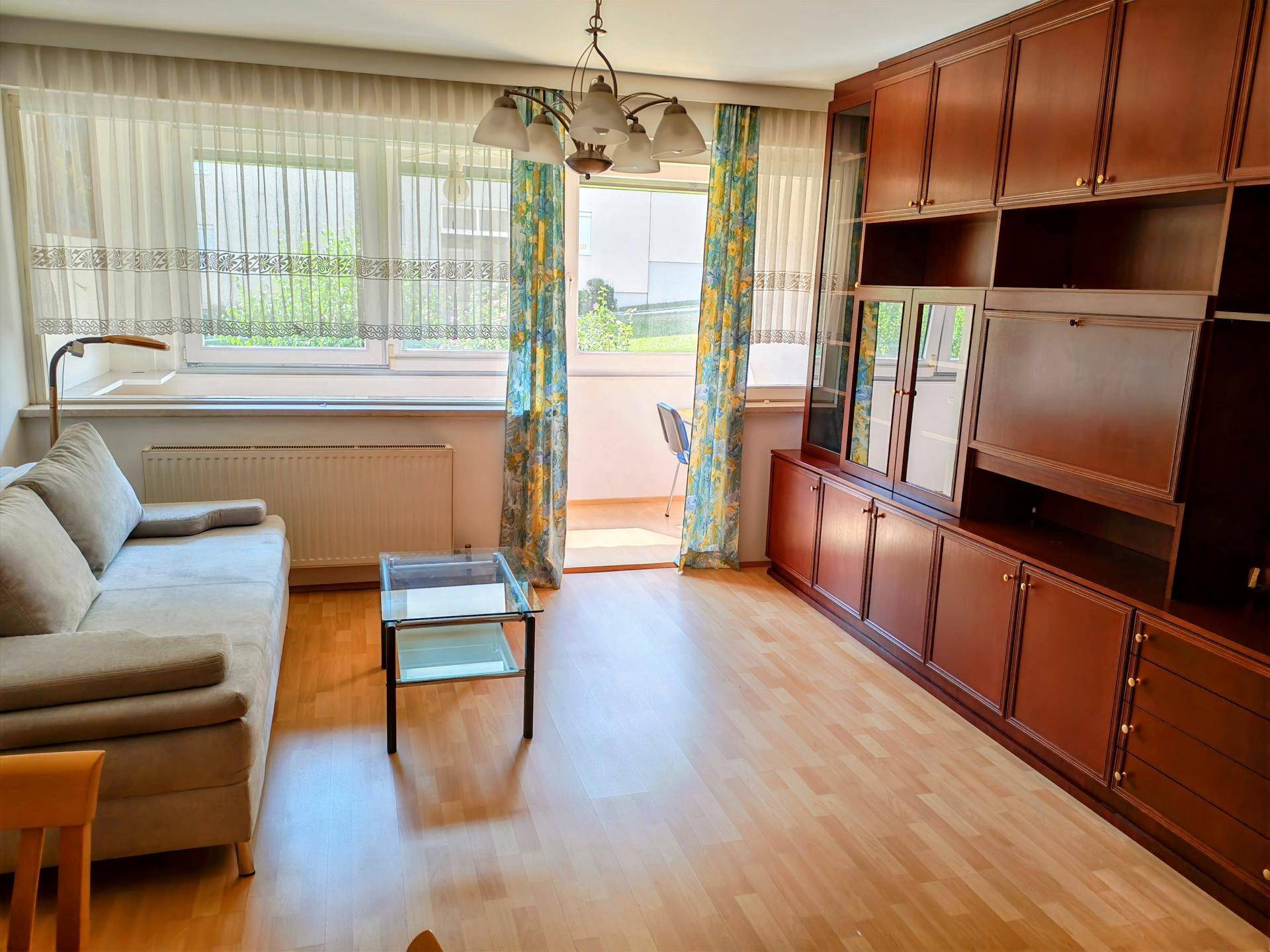 Gemütliches Wohnzimmer mit Sofa, Holzschrankwand und Zugang zu einem Balkon.