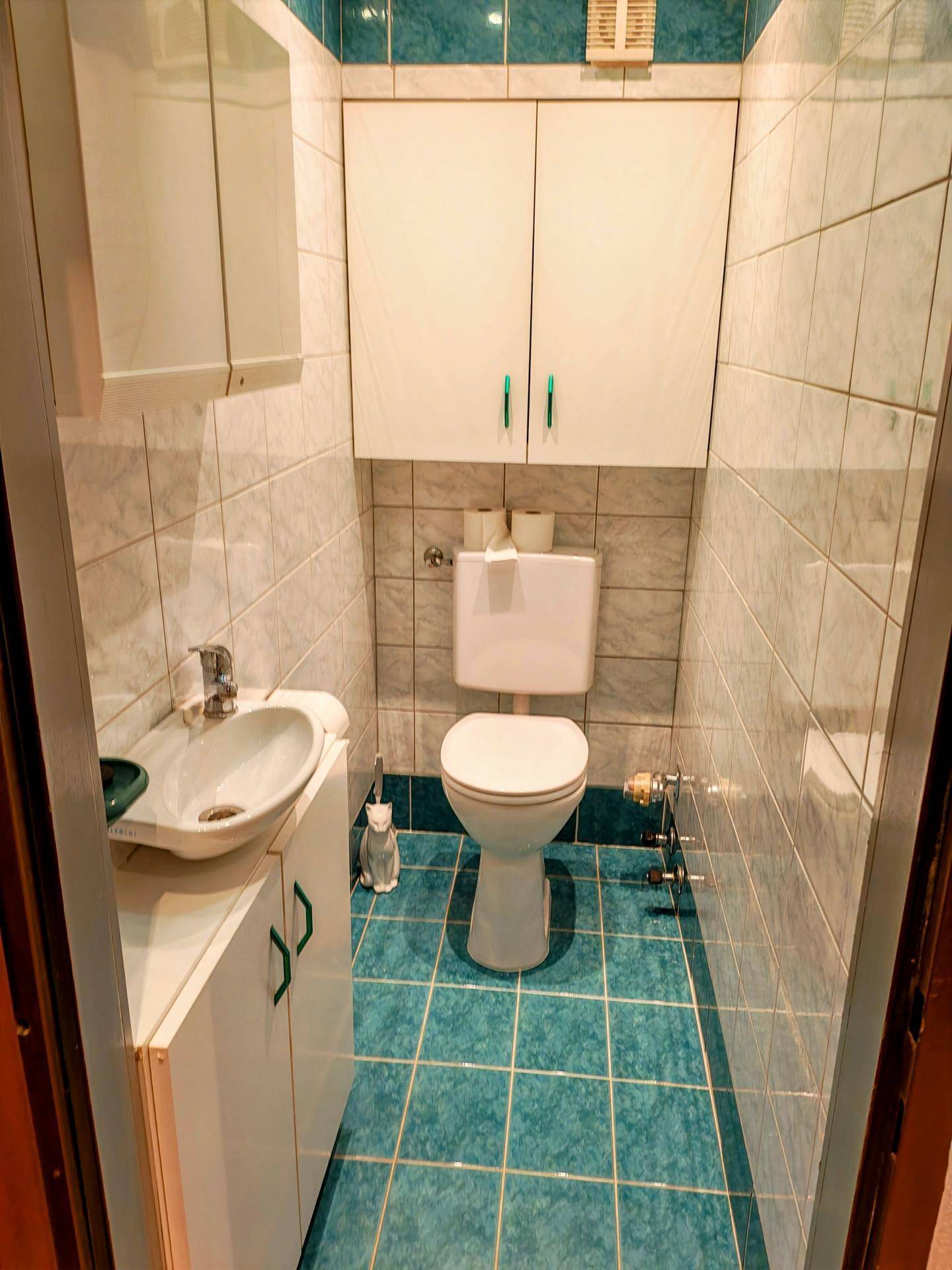 Kleines Gäste-WC mit Toilette, Waschbecken und Fliesen in Weiß und Türkis.