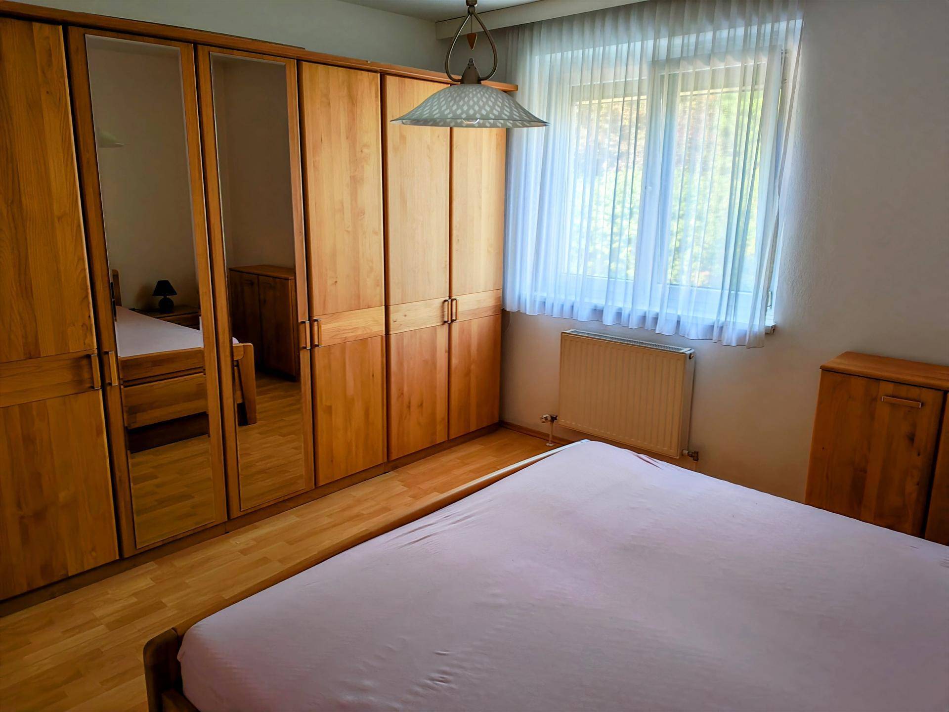 Schlafzimmer mit Doppelbett, großen Holzschränken mit Spiegeltüren und Fenster.