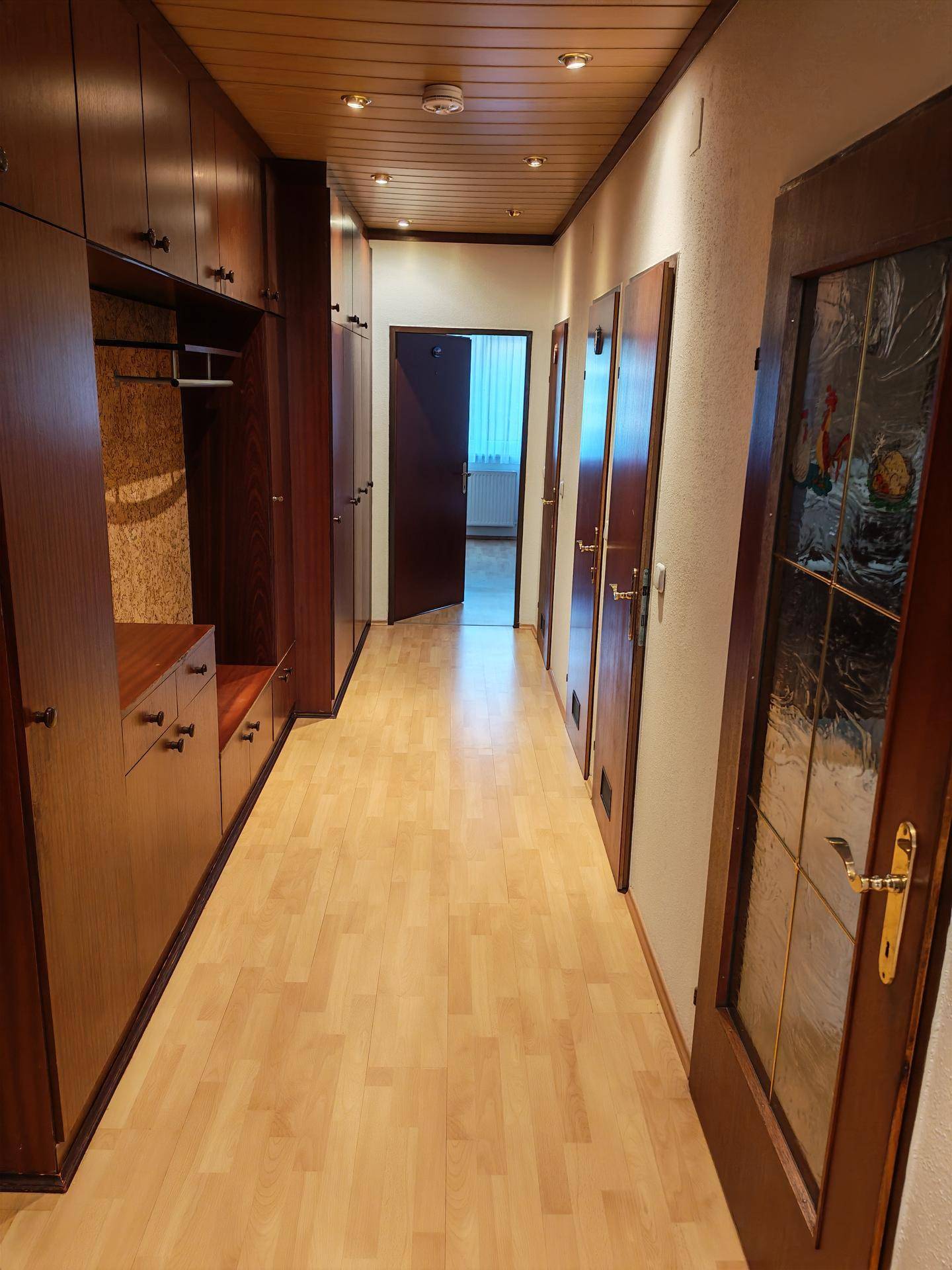 Langer Flur mit Einbauschränken aus Holz, Holzdecke und hellem Laminatboden.