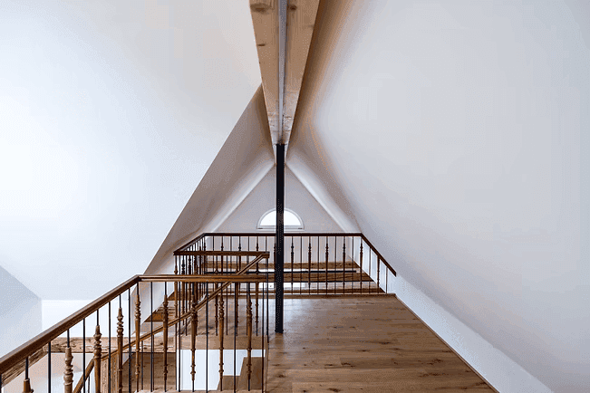 Dachgeschoss-Galerie mit Holzgeländer, sichtbarem Holzbalken und einem kleinen Rundfenster.