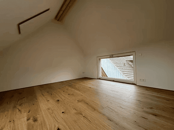 Dachgeschosszimmer mit Holzboden und einem Fenster, das einen Blick auf die Dächer bietet.