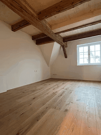 Geräumiges Schlafzimmer im Dachgeschoss mit Holzboden, sichtbaren Balken und Fenster.