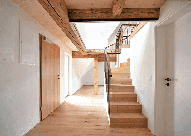 Heller Flur mit Holztreppe und sichtbaren Holzbalken, der zu weiteren Räumen führt.