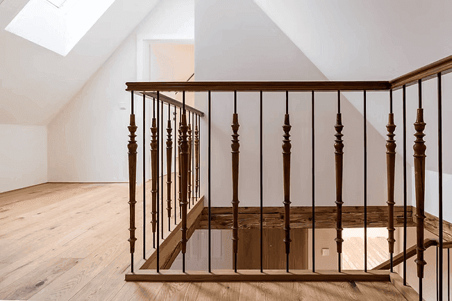 Detailansicht des Holzgeländers und der Treppe im hellen Dachgeschoss mit Dachfenster.
