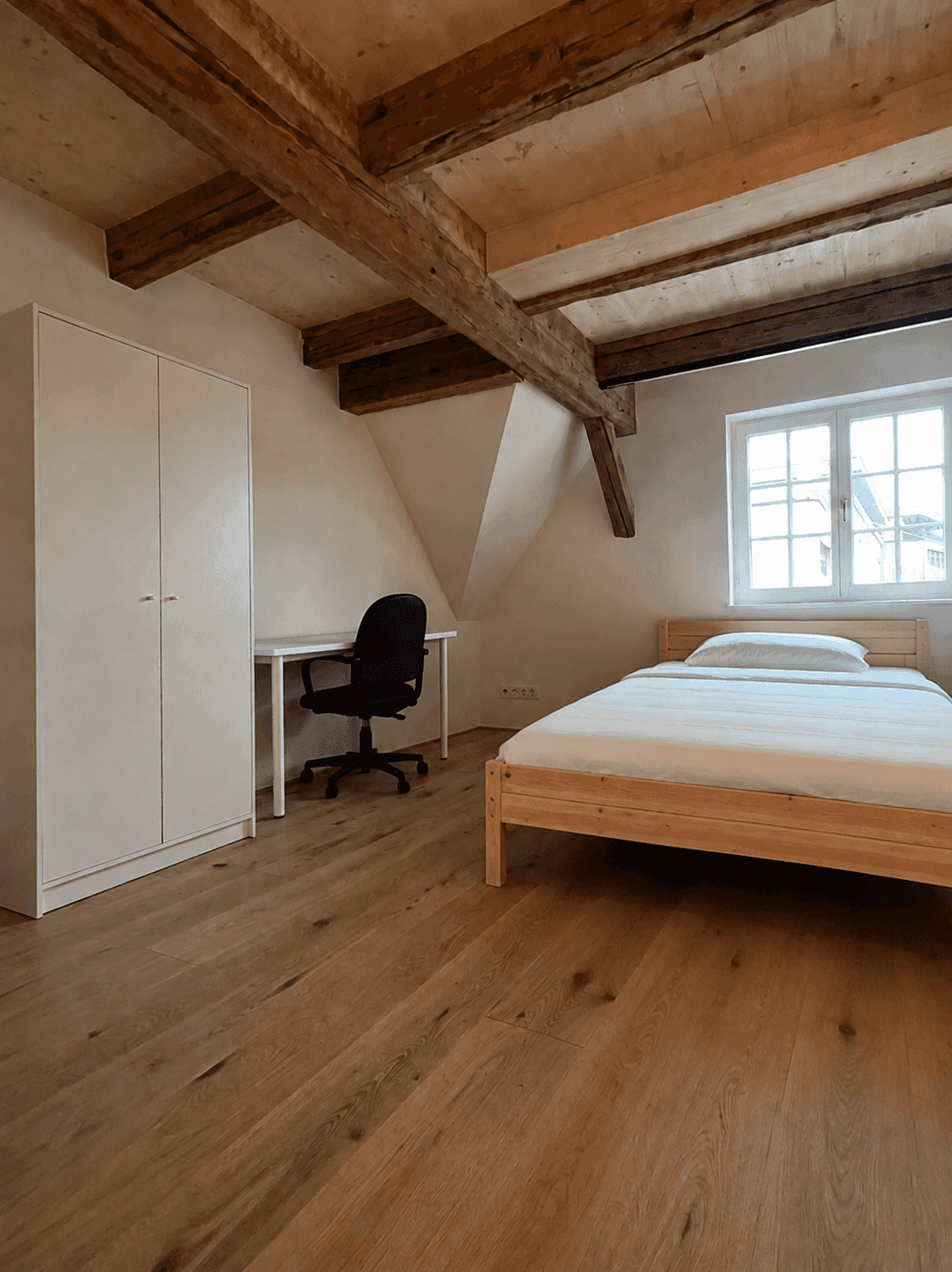 Gemütliches Schlafzimmer im Dachgeschoss mit Holzbett, Schrank und Schreibtisch.
