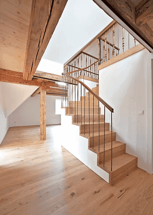 Geräumiger Flur mit Holztreppe und sichtbaren Holzbalken, der zu einem offenen Wohnbereich führt.