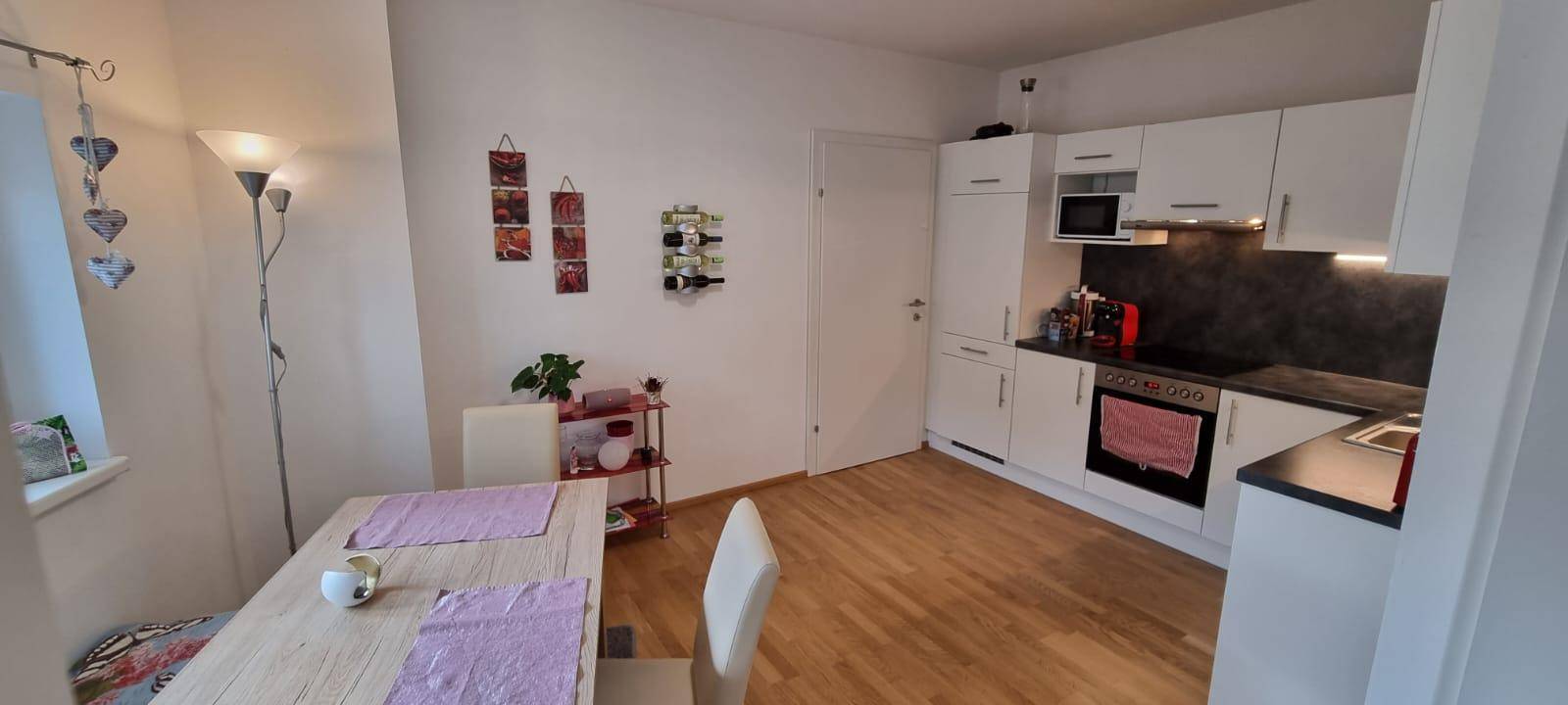 Offener Wohn- und Essbereich mit integrierter weißer Küche und Holzboden, ideal für geselliges Beisammensein.