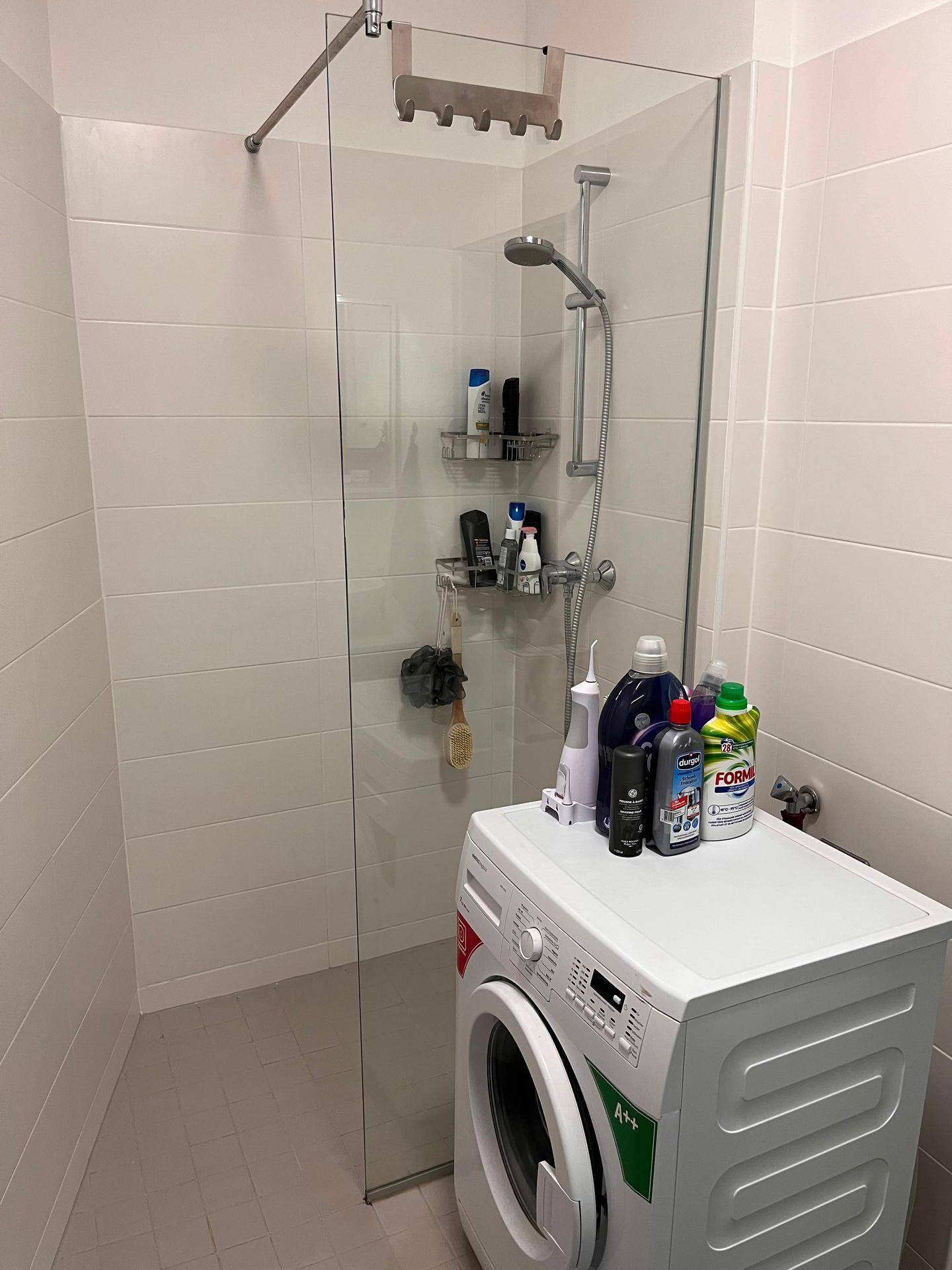 Helle Duschkabine mit Glasabtrennung und einer Waschmaschine im Badezimmer, praktisch und modern.