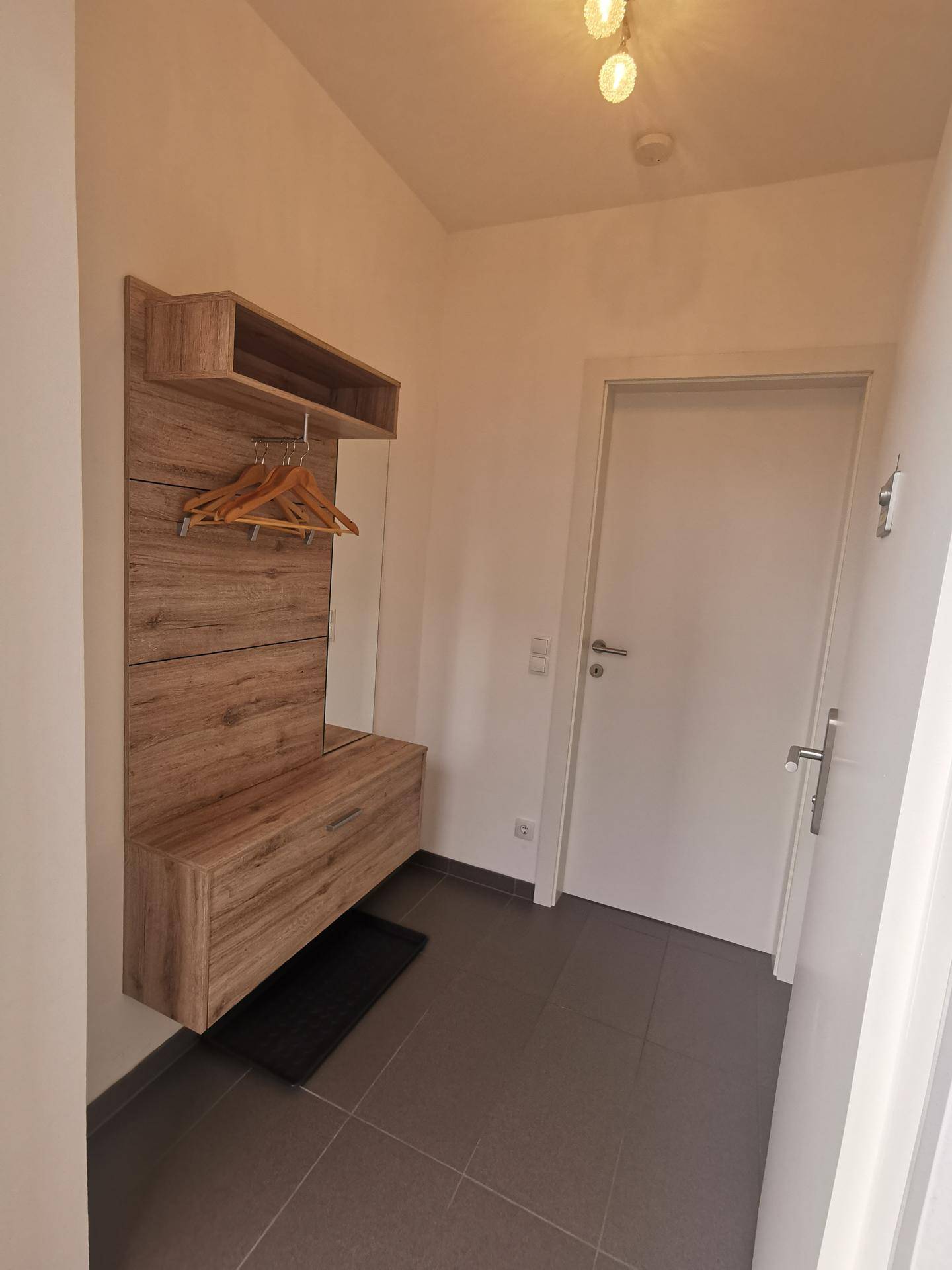 Heller Eingangsbereich mit modernem Garderobenmöbel aus Holz und dunklen Fliesen, einladend gestaltet.