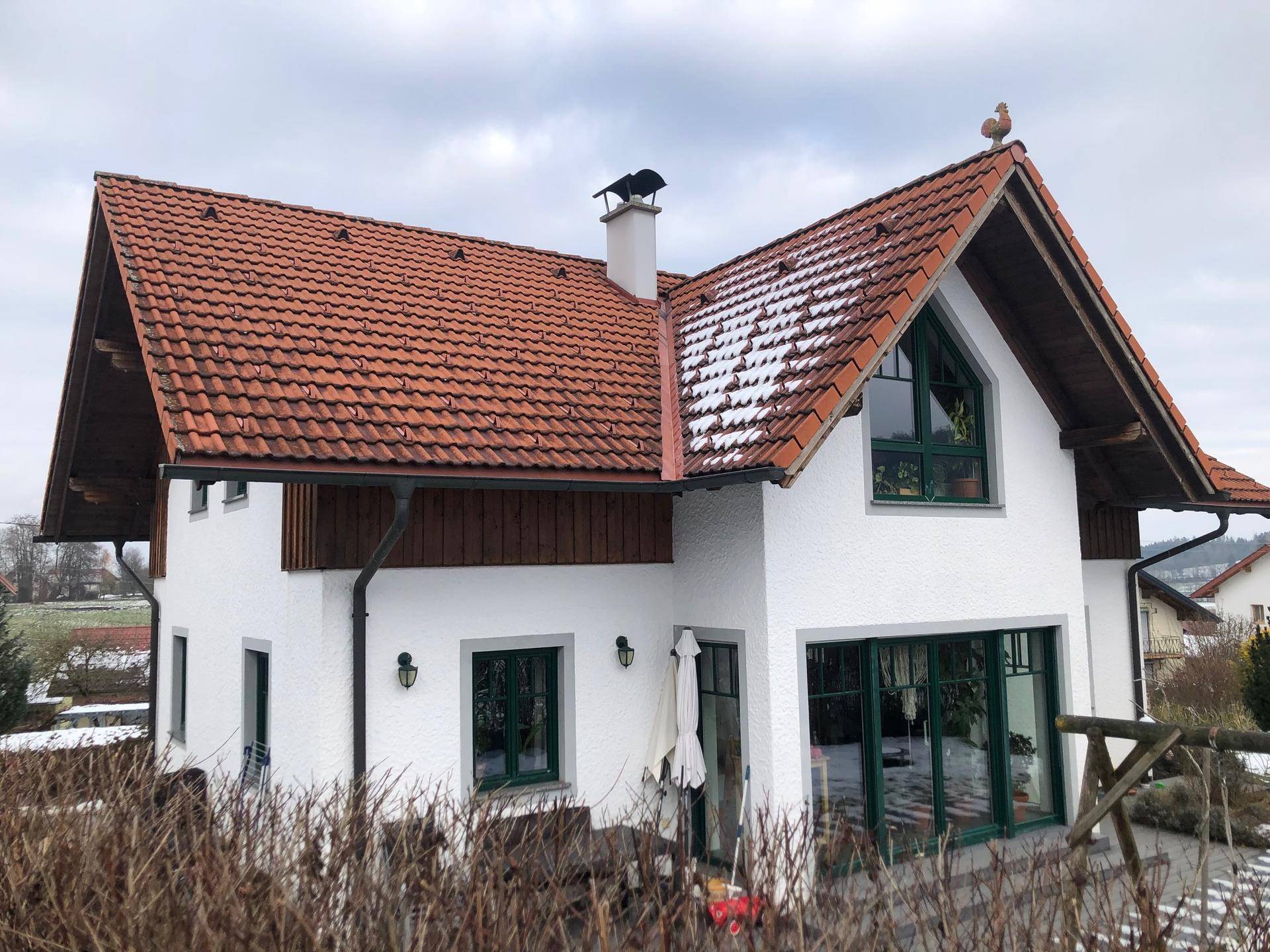 Charmantes Haus mit rotem Ziegeldach, großen Fenstern und einem Wetterhahn auf dem Giebel.