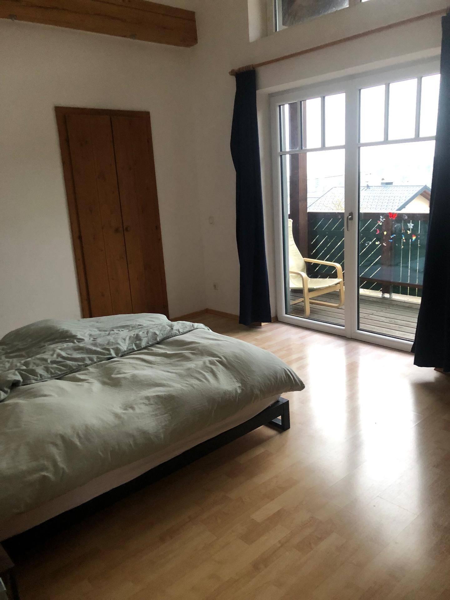 Schlafzimmer mit Holzboden, Holzbalken und Zugang zu einem Balkon.
