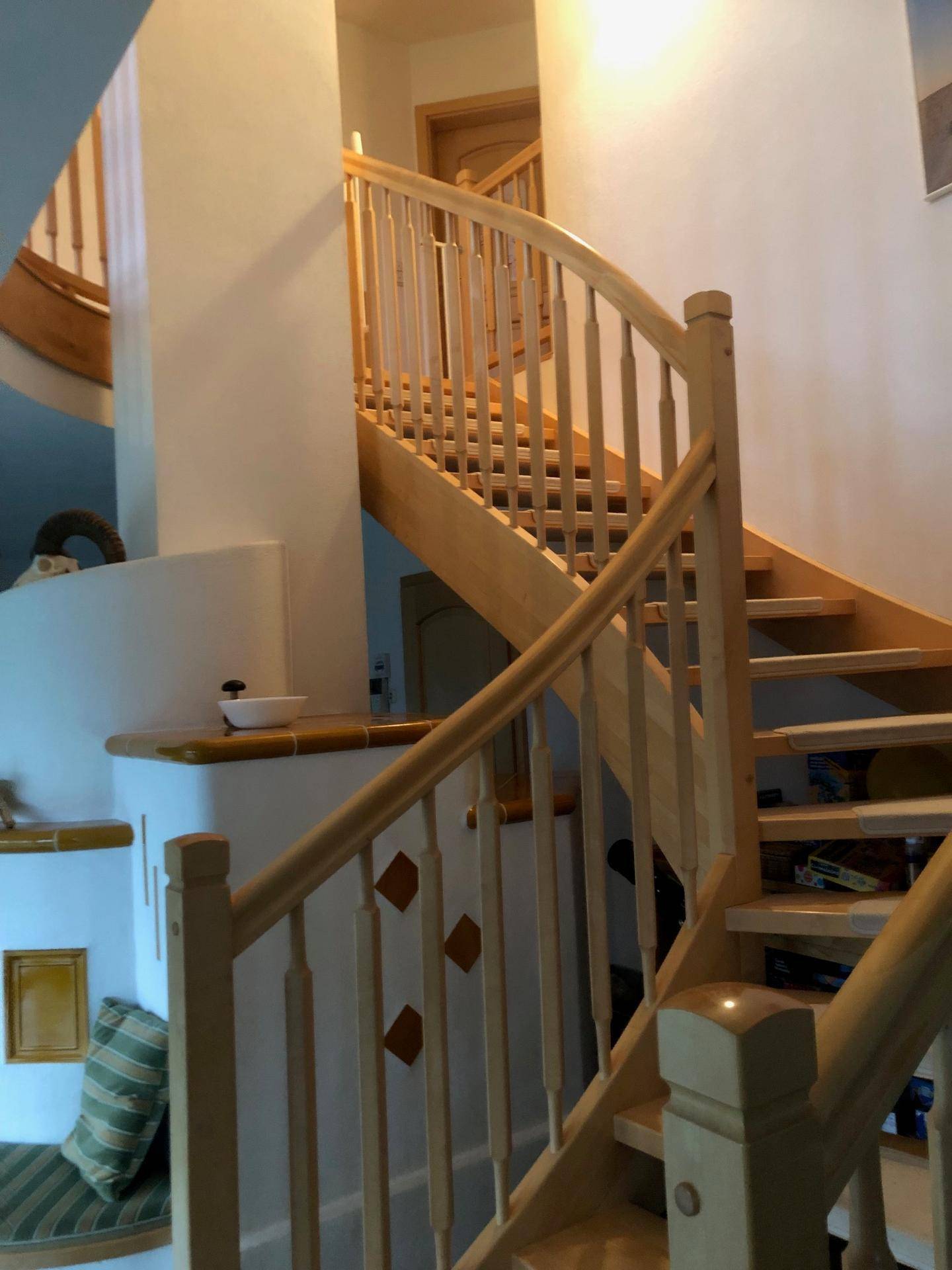 Helles Treppenhaus mit geschwungener Holztreppe und Geländer in hellem Holzton.