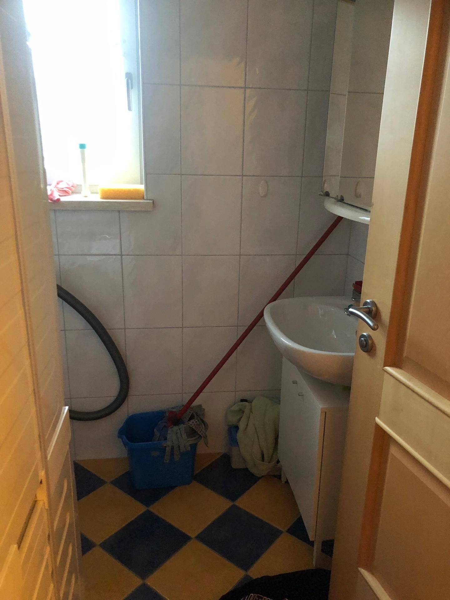 Kleiner Raum mit Waschbecken, Fenster und auffälligem gelb-blau kariertem Boden.