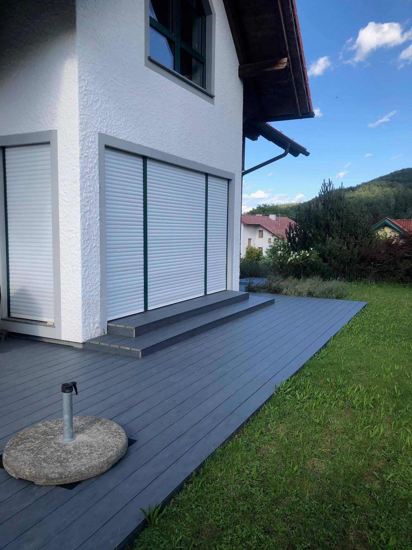Moderne Terrasse aus dunklem Holzverbundwerkstoff mit Blick auf die grüne Umgebung.