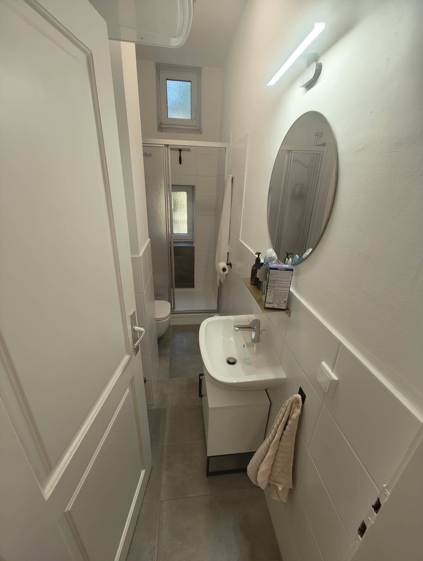 Modernes Badezimmer mit Dusche, Waschbecken, Spiegel und einem kleinen Fenster.
