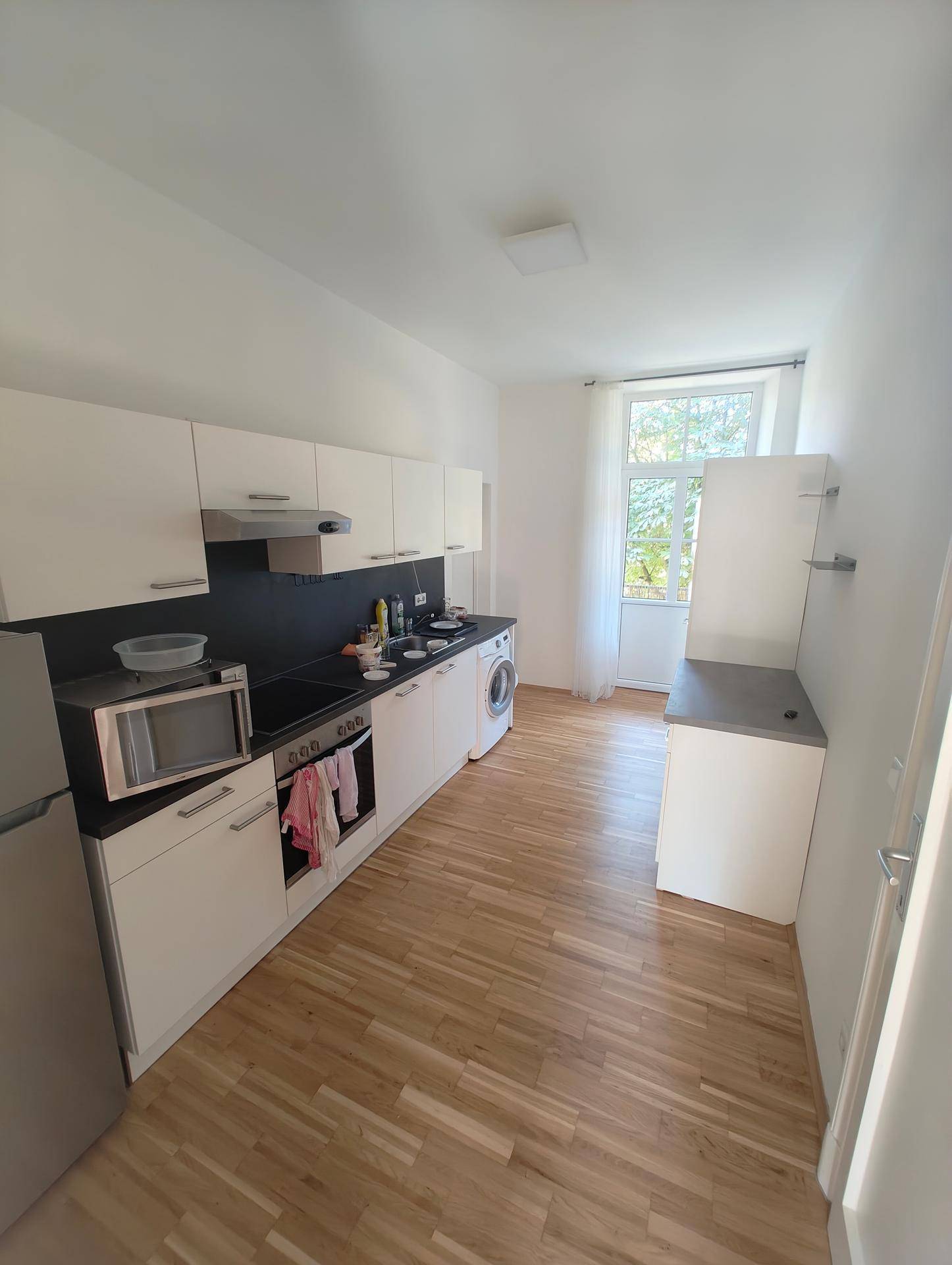 Funktionale Küche mit weißen Schränken, Holzparkett und Zugang zum Balkon.