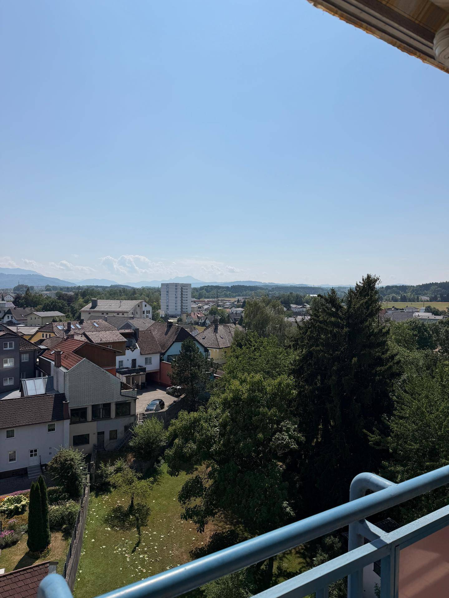 Weitläufiger Ausblick vom Balkon über eine Stadtlandschaft mit viel Grün und Bergen im Hintergrund.