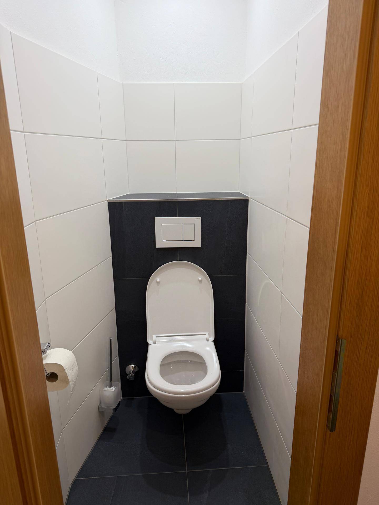 Kleines separates WC mit weißen und schwarzen Fliesen sowie einer Wandtoilette.