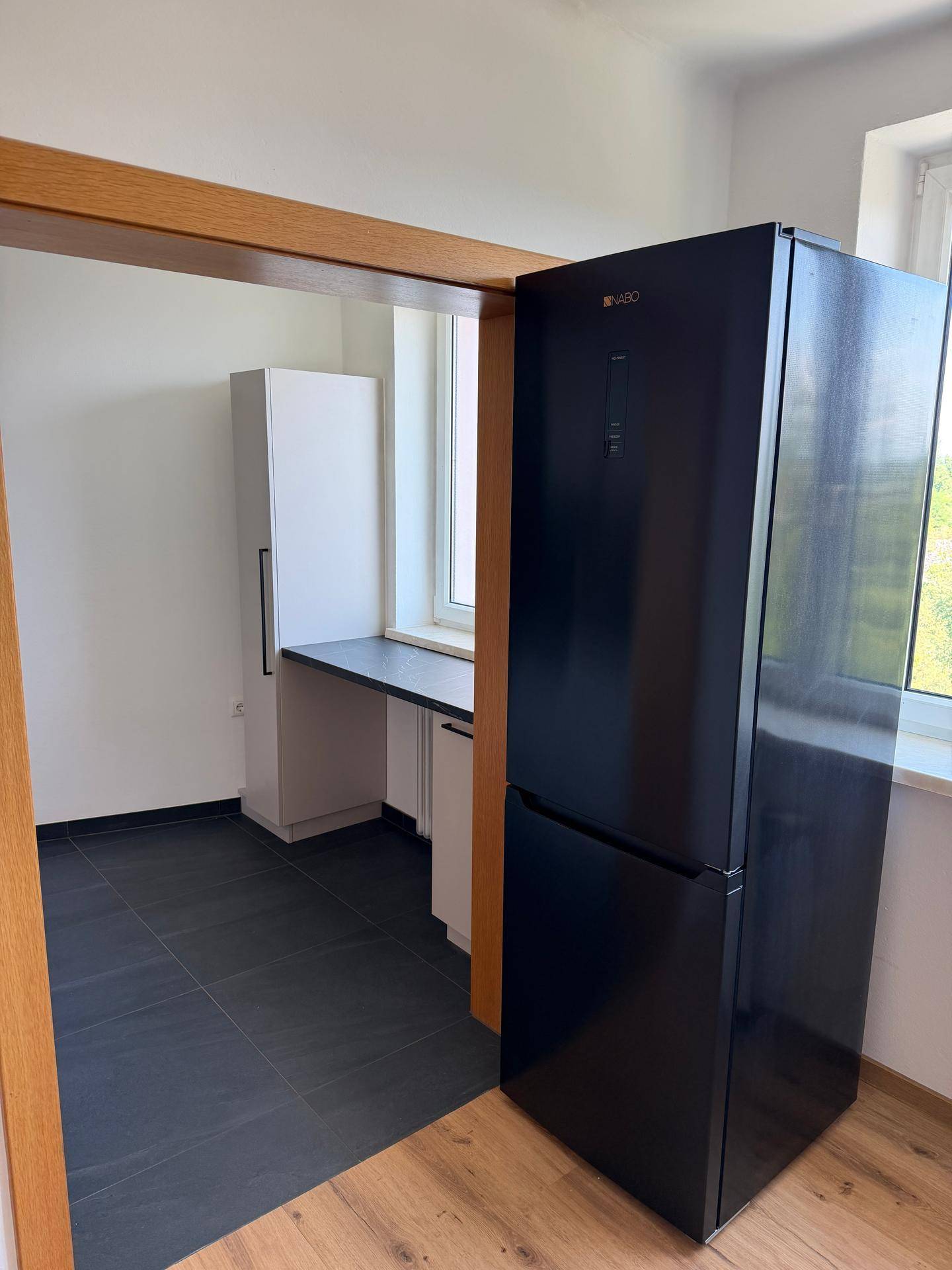 Küchenbereich mit dunklen Fliesen, Arbeitsplatte und einem großen schwarzen Kühlschrank.