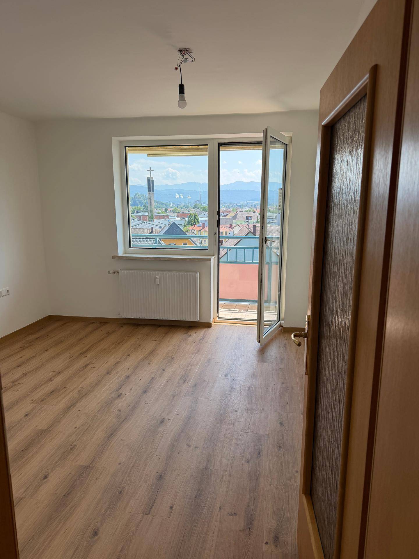 Heller Raum mit Laminatboden und Zugang zu einem Balkon mit Bergblick.
