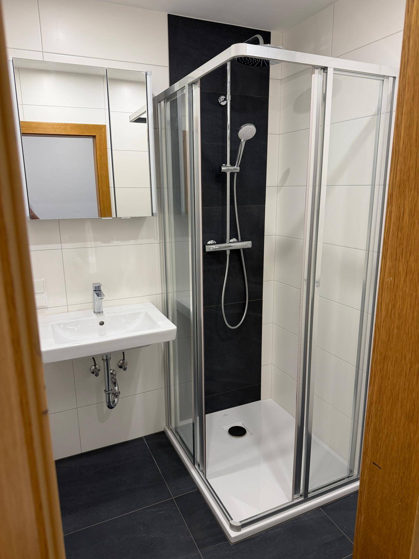 Modernes Badezimmer mit Dusche, Waschbecken und Spiegel, gefliest in Schwarz und Weiß.