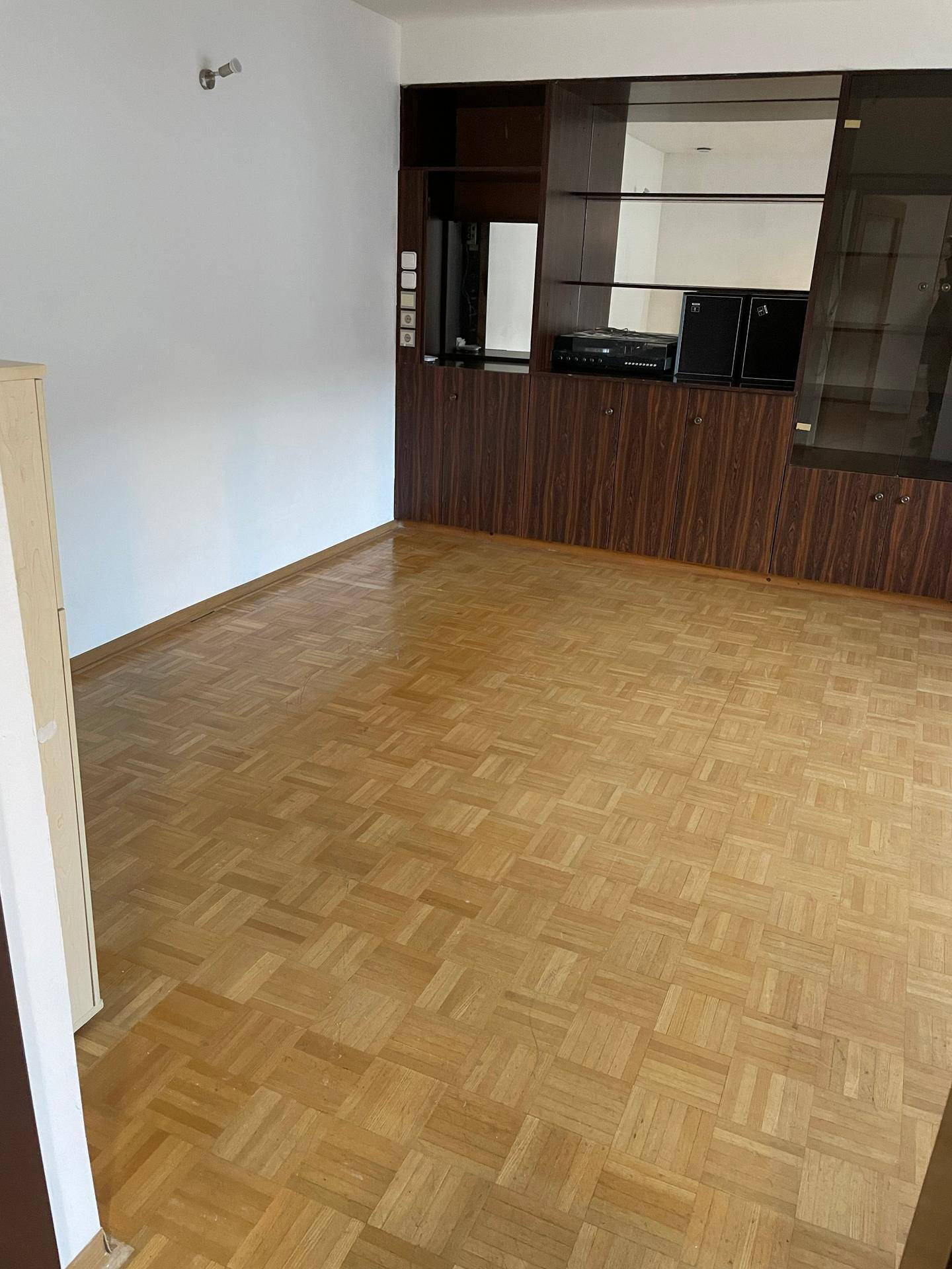 Geräumiges Wohnzimmer mit Parkettboden und einer großen, dunklen Einbauwand mit Spiegelelementen.