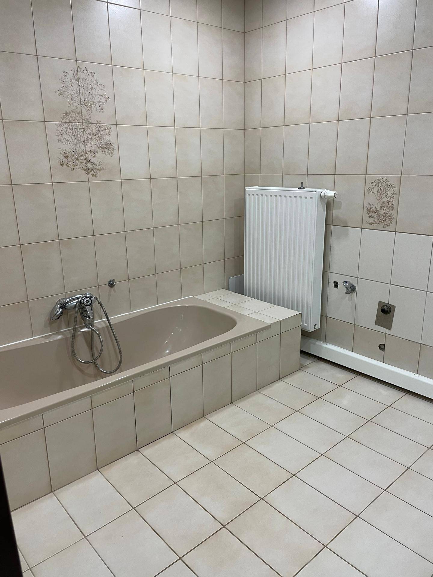 Badezimmer mit beigefarbenen Fliesen, einer eingebauten Badewanne und einem Heizkörper, klassisch gestaltet.