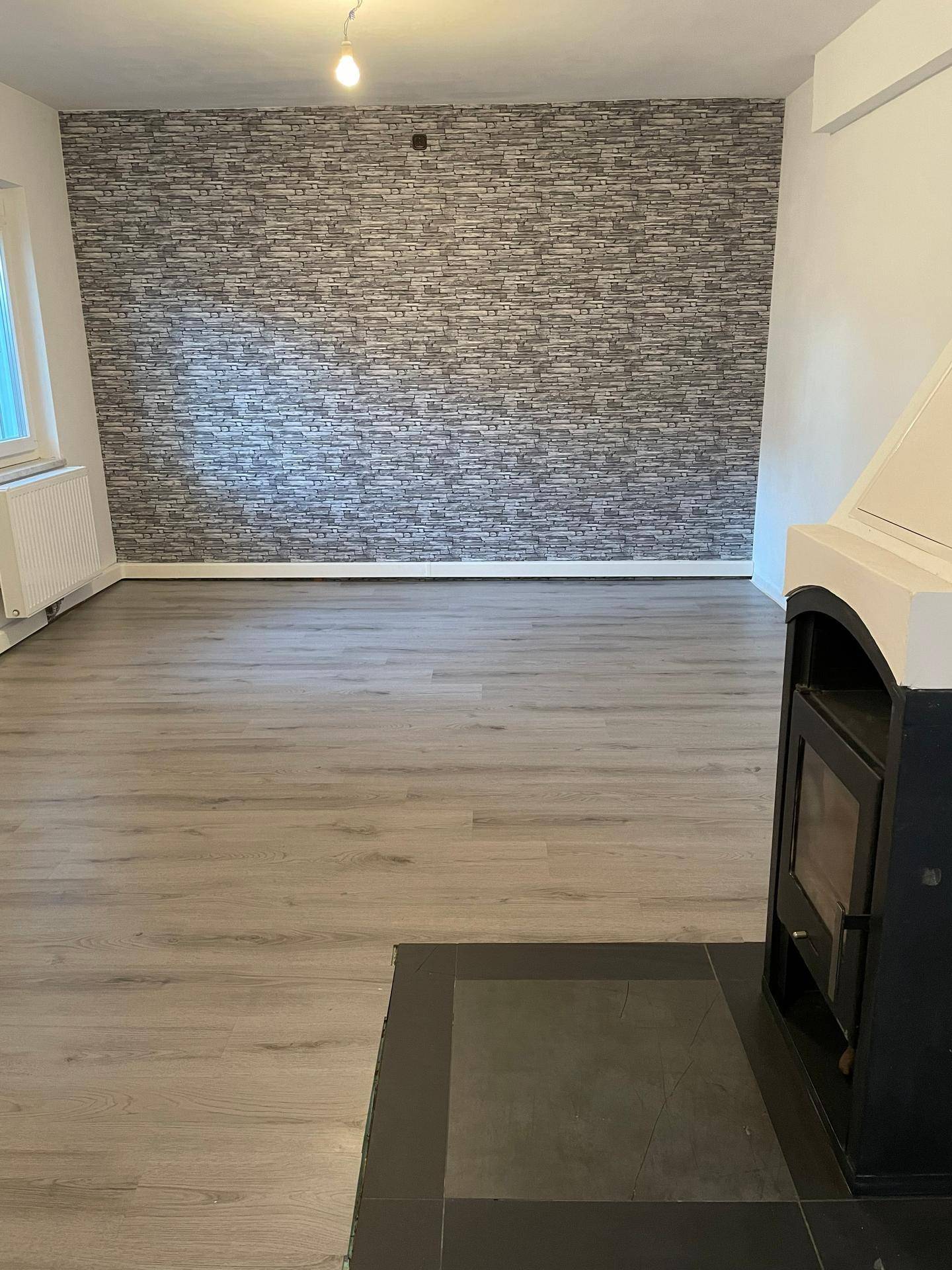 Gemütliches Wohnzimmer mit hellem Laminatboden, einer Akzentwand und einem modernen Holzofen für Wärme.