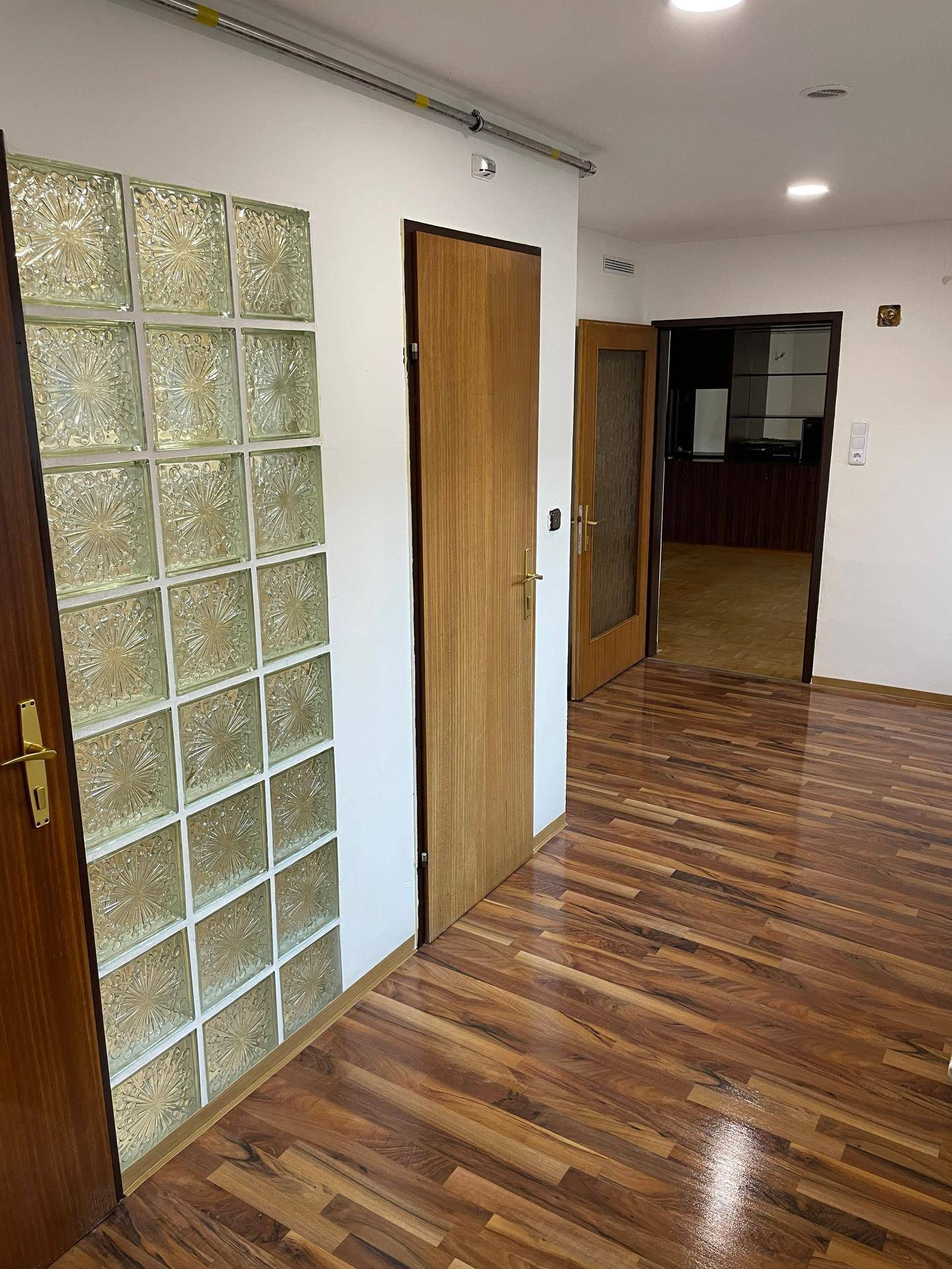 Heller Flur mit dunklem Laminatboden, einer dekorativen Glasbausteinwand und Holztüren, die zu weiteren Räumen führen.
