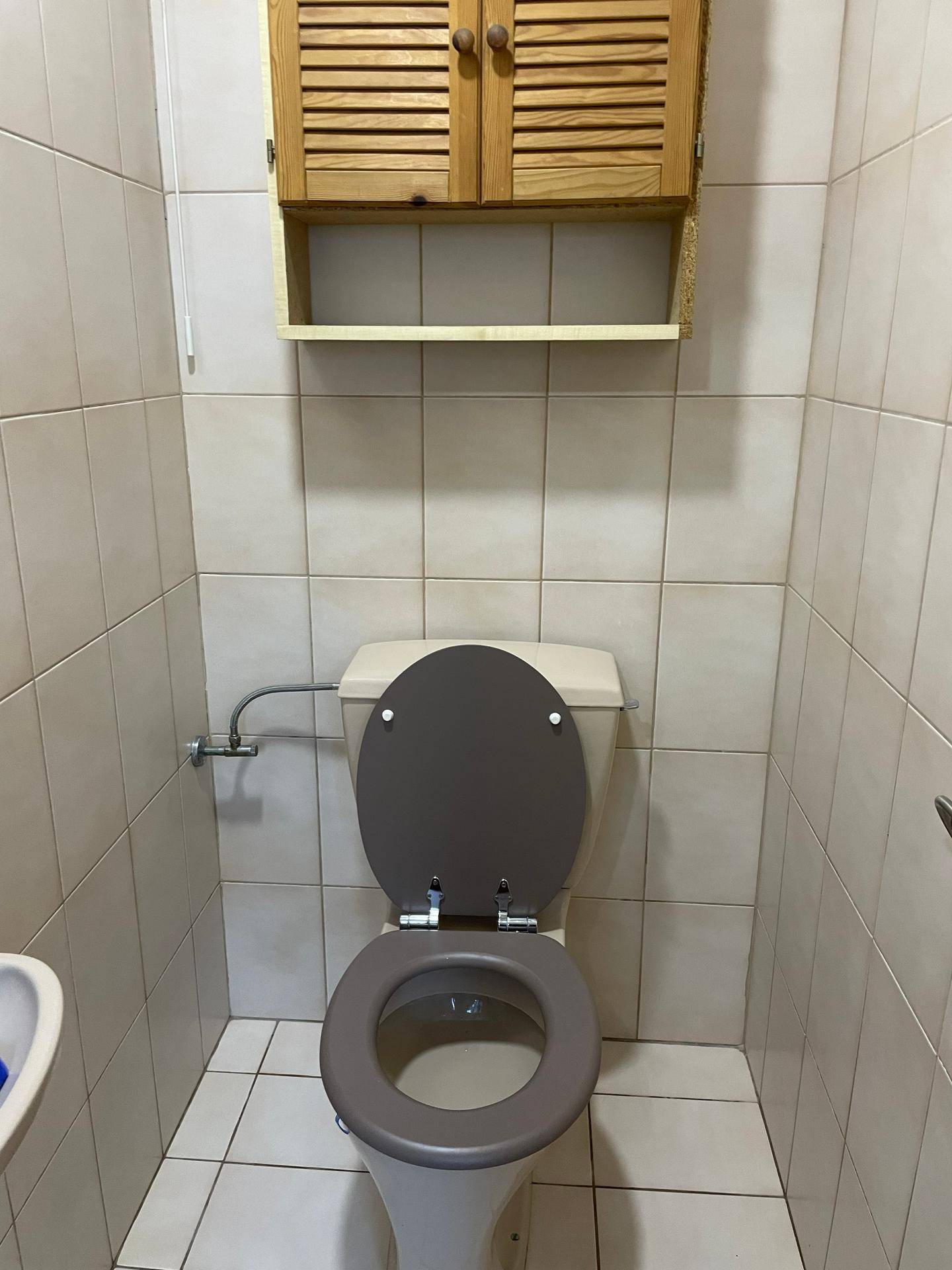 Separates WC mit beigefarbenen Fliesen, einer Toilette und einem kleinen Holzschrank für zusätzlichen Stauraum.