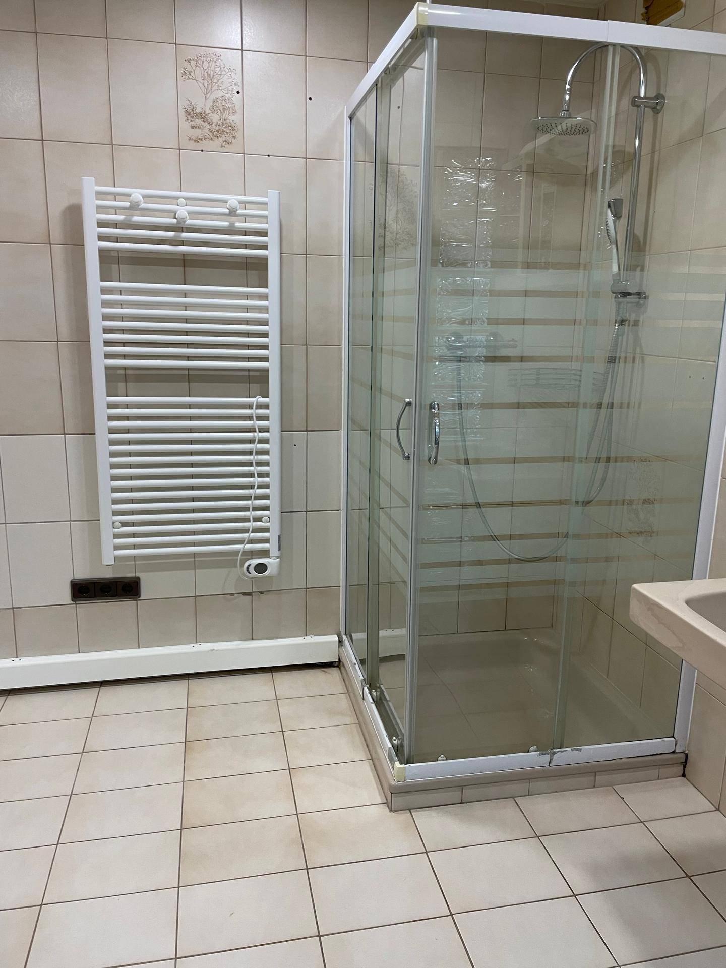 Badezimmer mit beigefarbenen Fliesen, einer Duschkabine und einem praktischen beheizten Handtuchhalter.