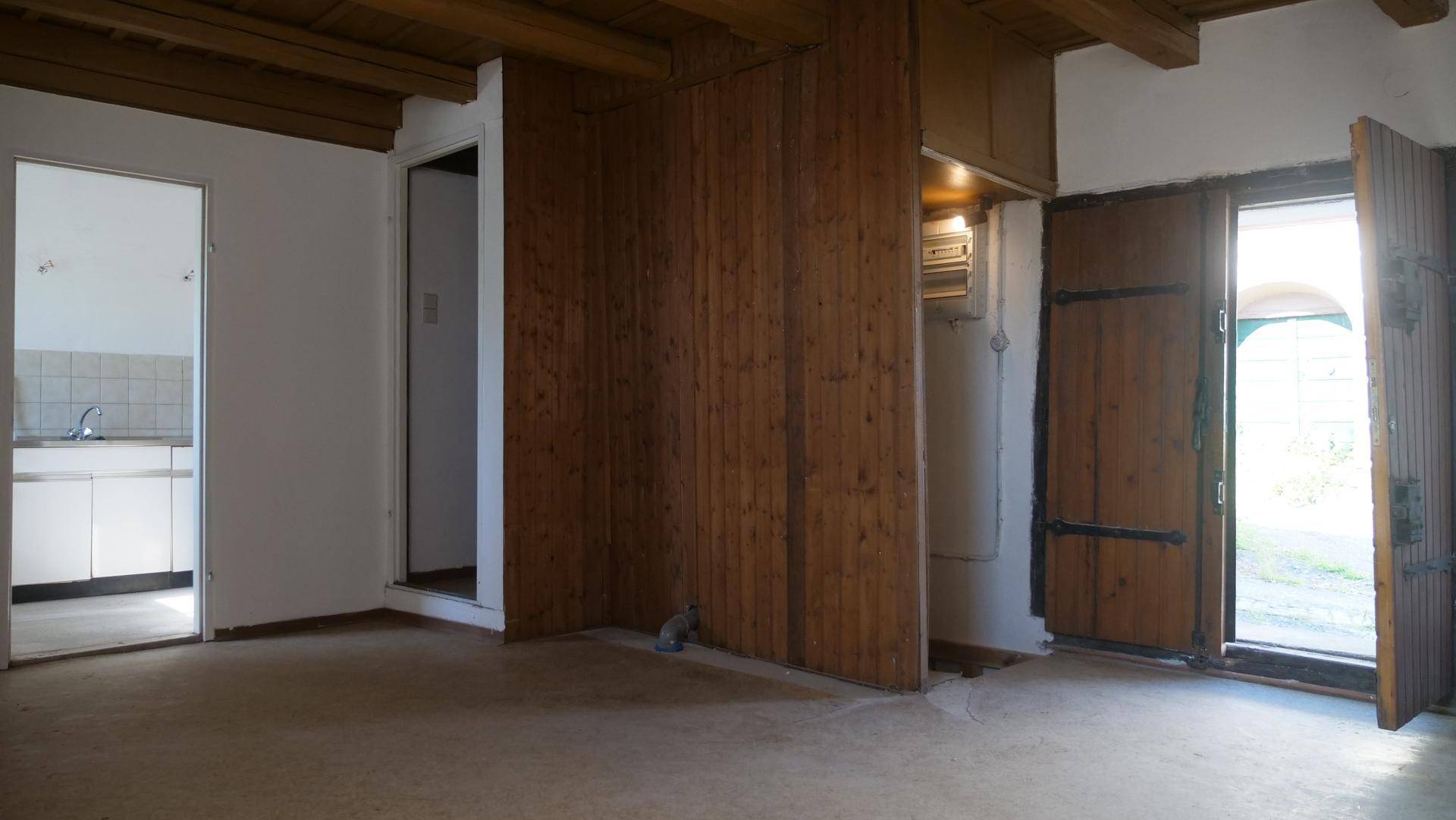 Geräumiger Innenraum mit Holzbalkendecke, Holzvertäfelung und Zugang zu einem Nebenraum und ins Freie.