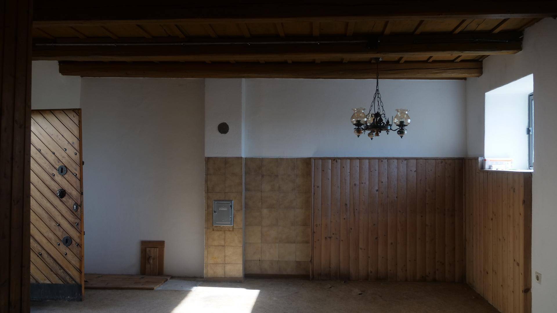 Innenraum mit sichtbaren Holzbalken an der Decke, Holzvertäfelung und einem Kronleuchter.