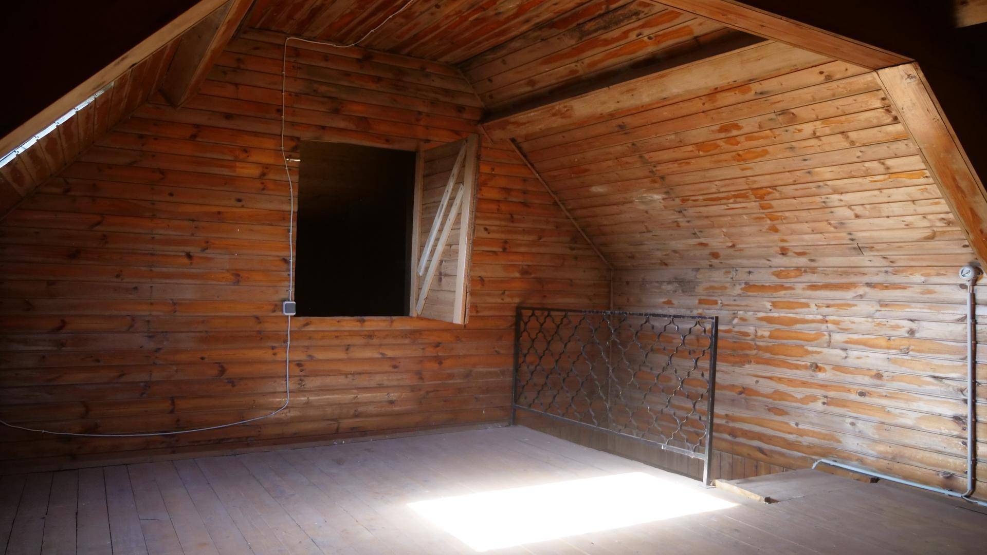 Dachbodenraum mit schrägen Holzdecken, Holzvertäfelung und einem Fenster mit Blick ins Grüne.