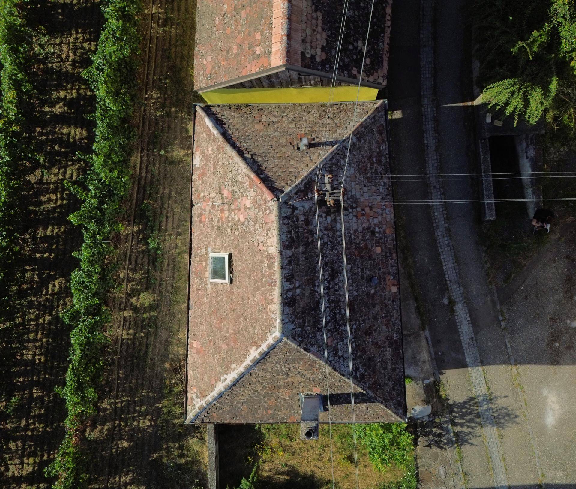 Vogelperspektive des Gebäudes mit Ziegeldach und Dachfenster, umgeben von Weinbergen und einer Straße.