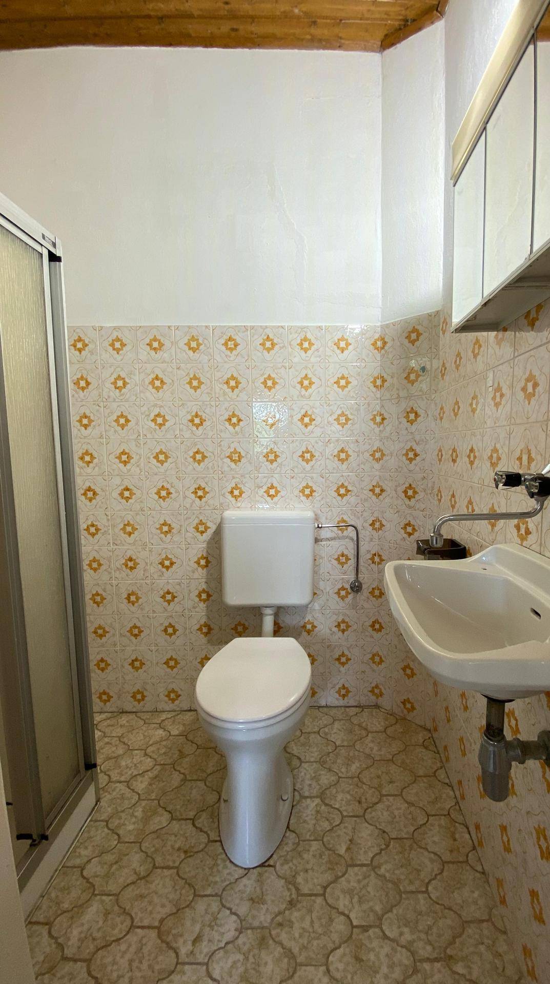 Kleines Badezimmer mit gemusterten Fliesen, Toilette, Waschbecken und Duschkabine.