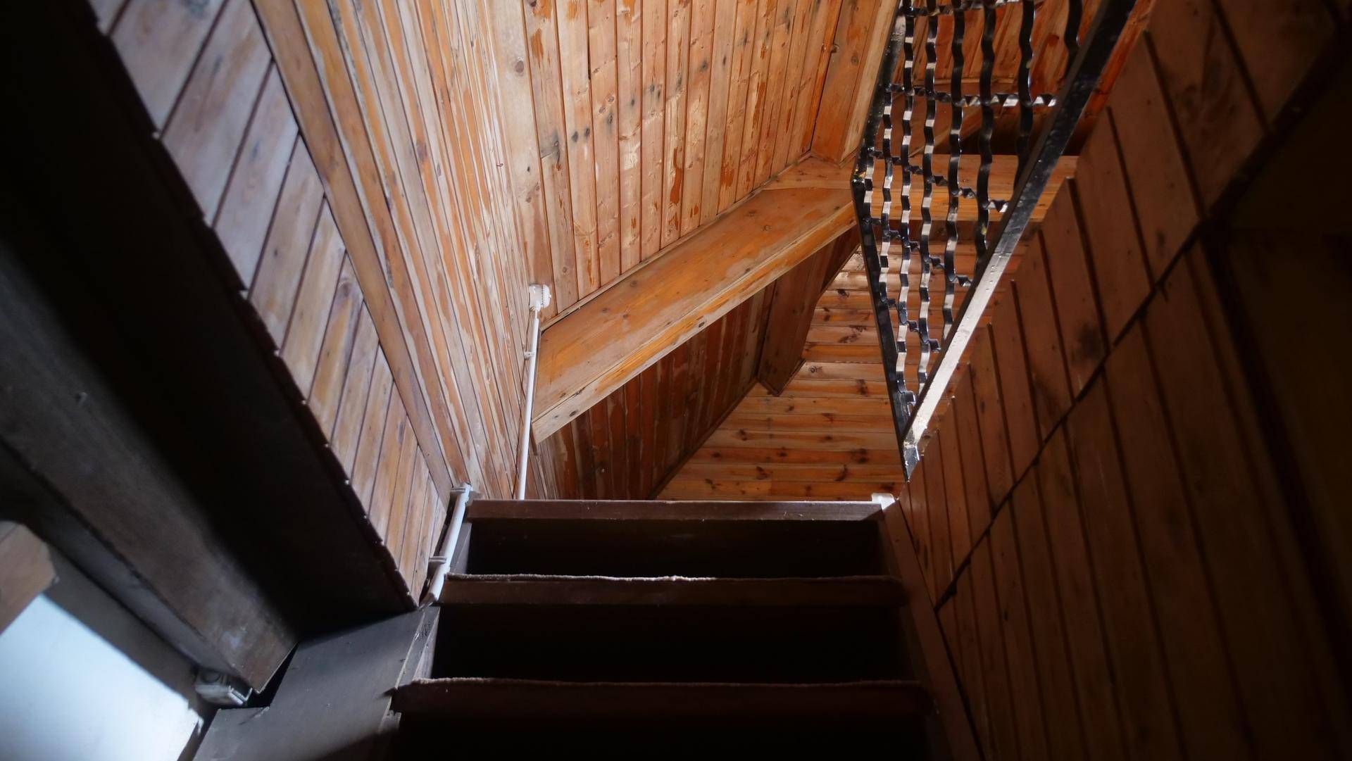 Holztreppe führt nach oben, umgeben von Holzvertäfelung an Wänden und Decke.