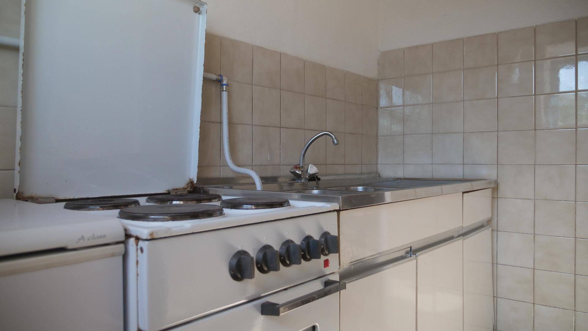 Kleine, einfache Küche mit Spüle, Elektroherd und beigefarbenen Fliesen an der Wand.