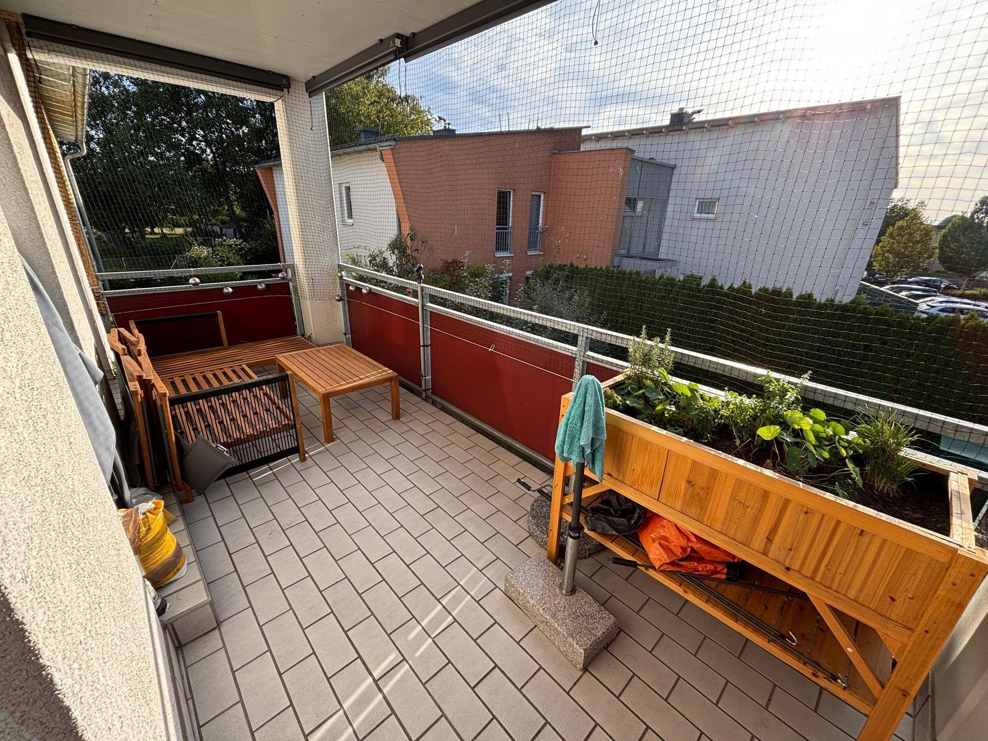 Möblierter Balkon mit Fliesenboden, Holztisch und Pflanzenkästen, ideal für entspannte Stunden.
