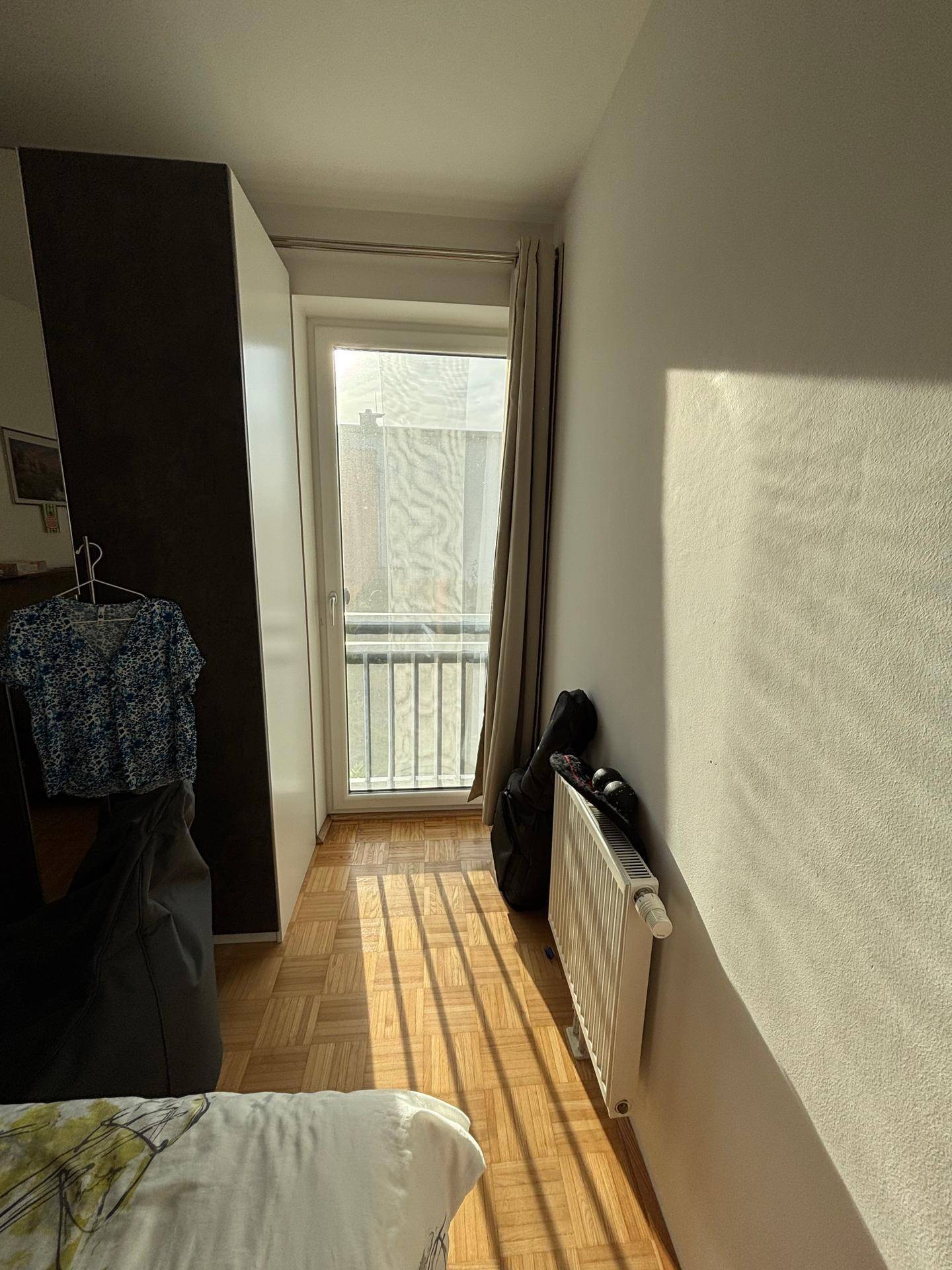Raum mit Parkettboden und einem französischen Balkon, der für zusätzliche Belüftung sorgt.