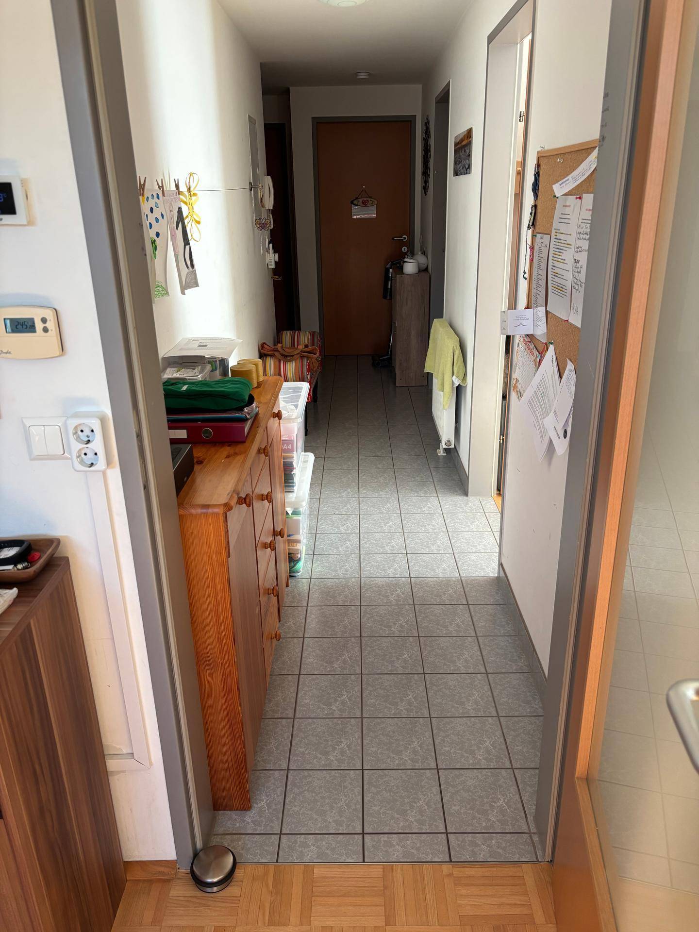 Schmaler Flur mit hellen Fliesen und einem Holzschrank, der zu weiteren Räumen führt.
