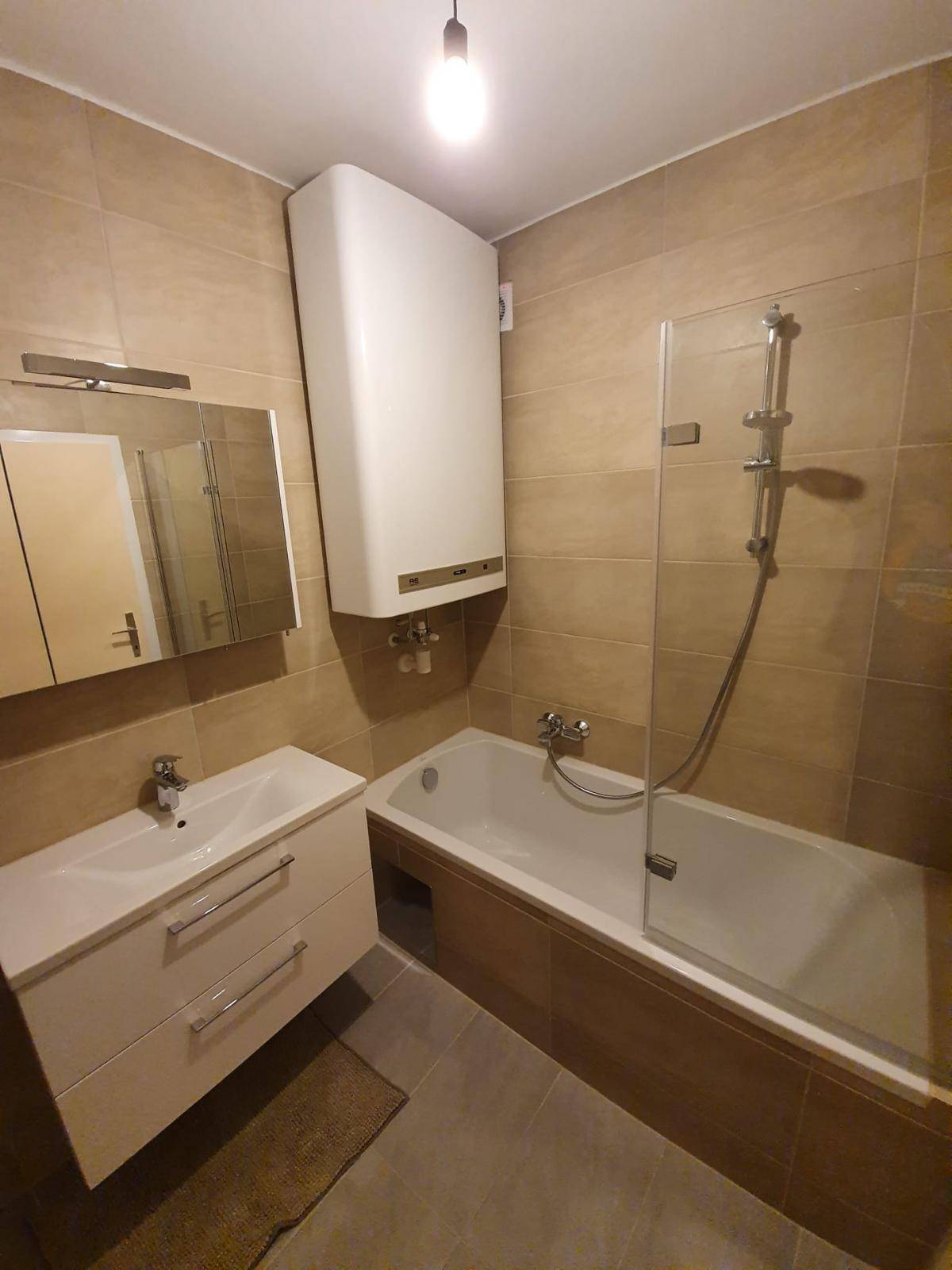Badezimmer mit Badewanne, Duschabtrennung, Waschbecken und beigefarbenen Fliesen an Wänden und Boden.