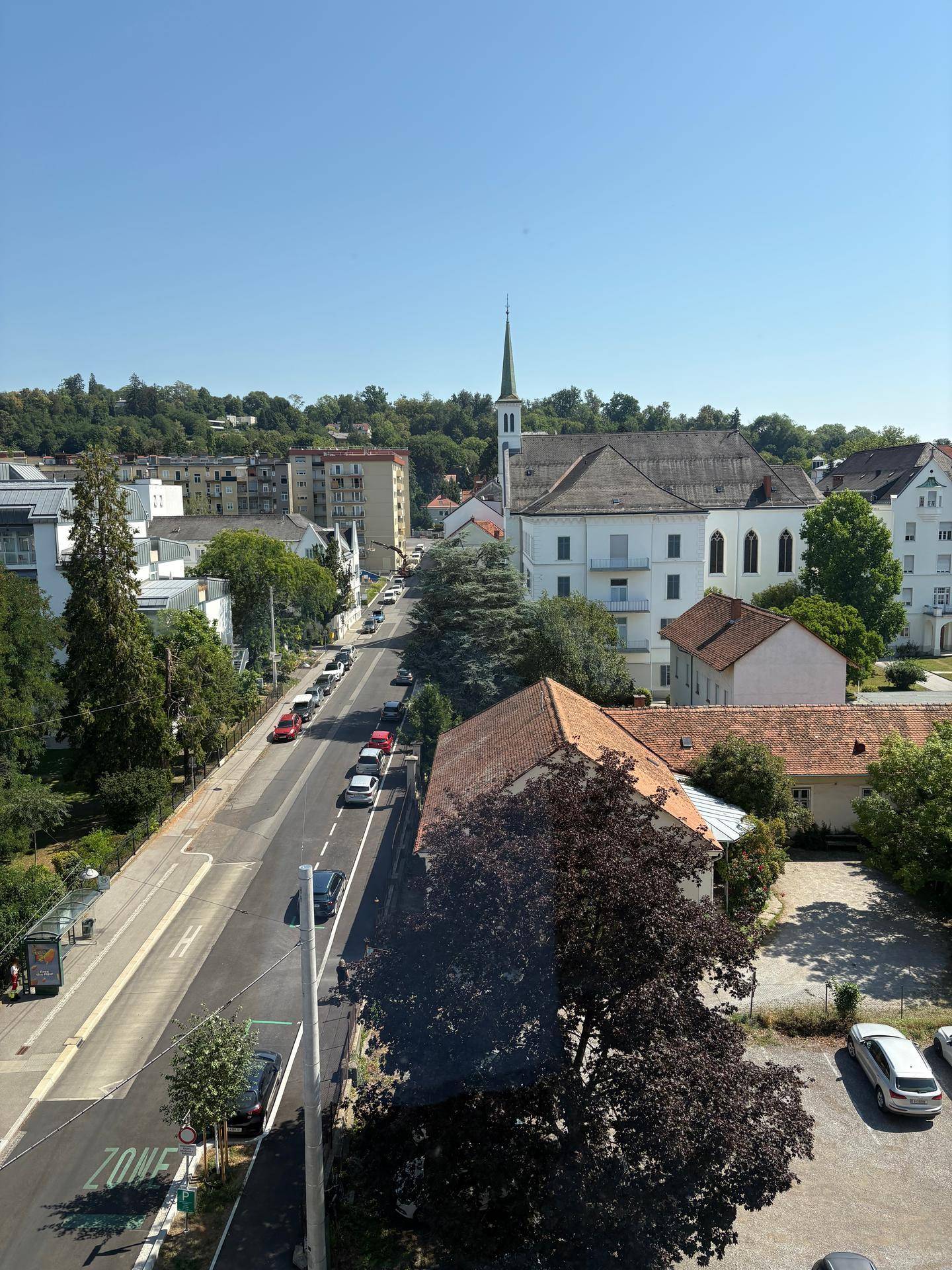 Panoramablick über die Stadt mit Straße, Gebäuden und viel Grün unter blauem Himmel.
