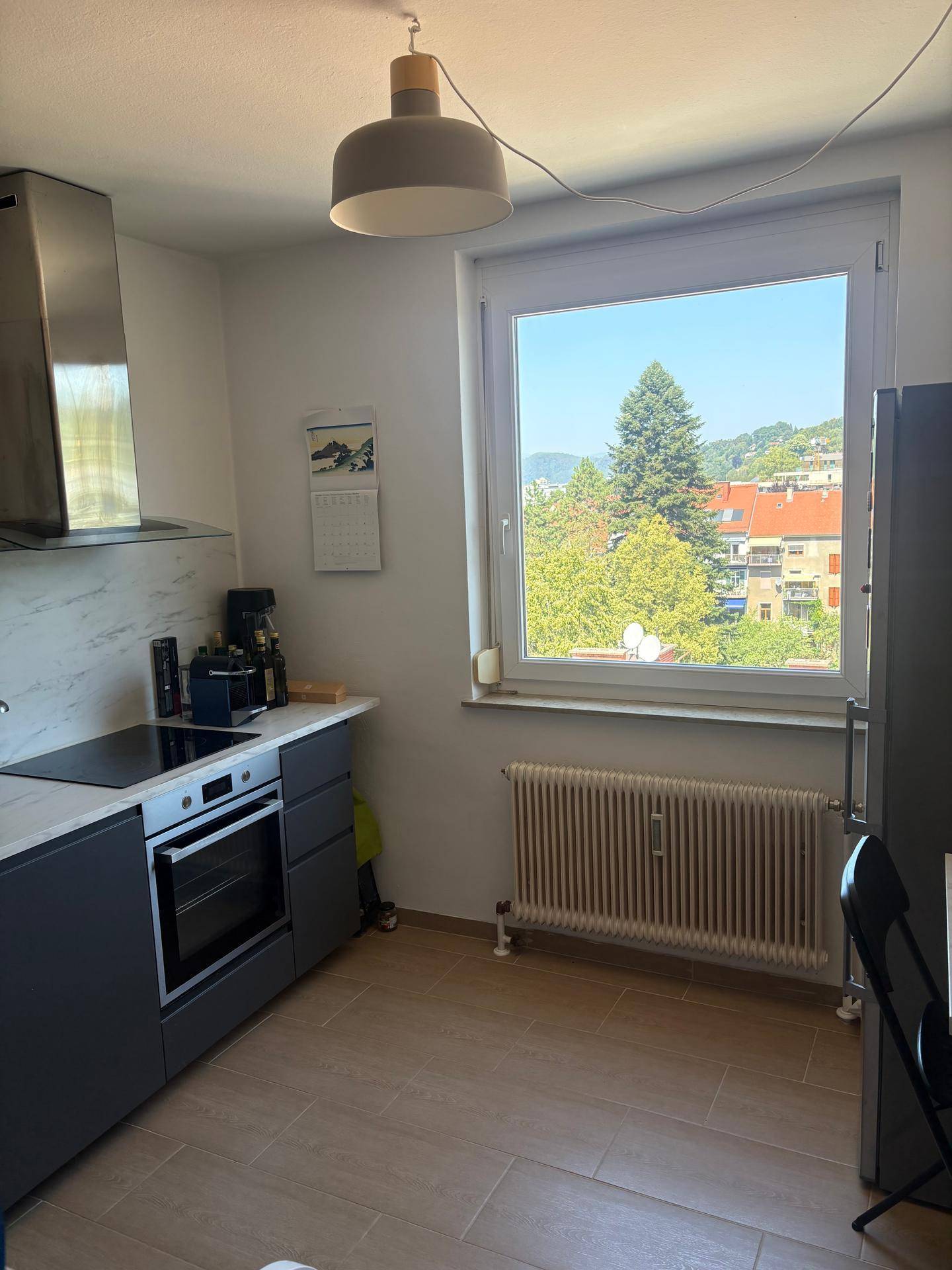 Moderne Küche mit grauen Unterschränken, Induktionskochfeld und Fenster mit Ausblick ins Grüne.