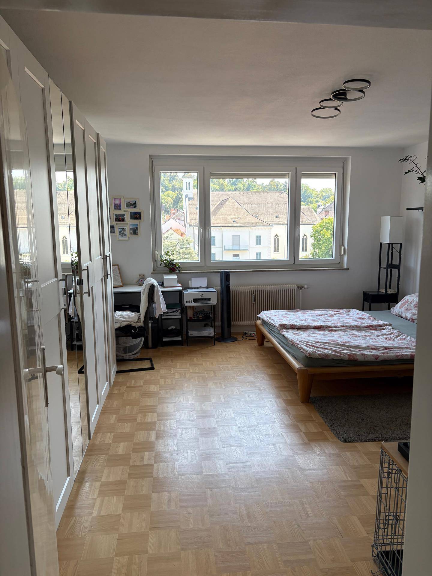 Geräumiges Schlafzimmer mit Parkettboden, großem Fenster und integrierten Kleiderschränken.