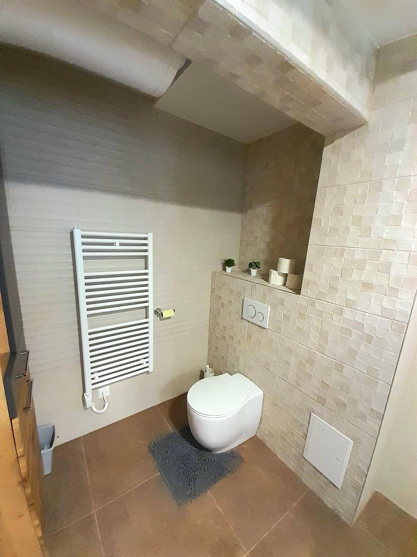 Modern gefliestes WC mit wandhängender Toilette und beheiztem Handtuchhalter.