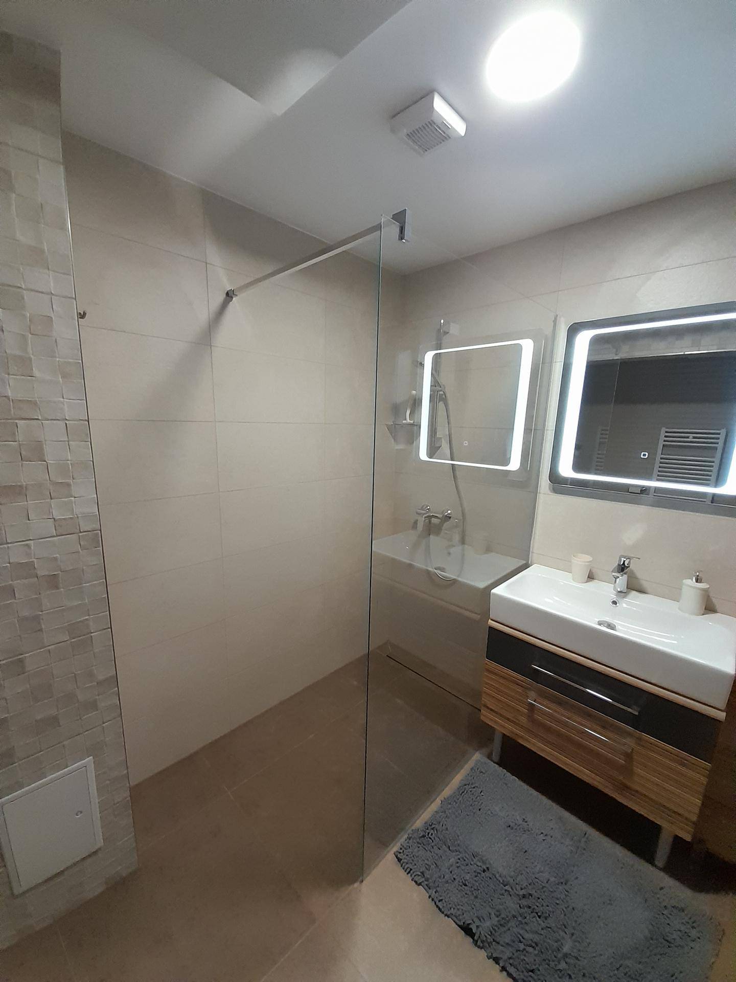 Helles Badezimmer mit begehbarer Dusche, modernem Waschtisch und beleuchteten Spiegeln.