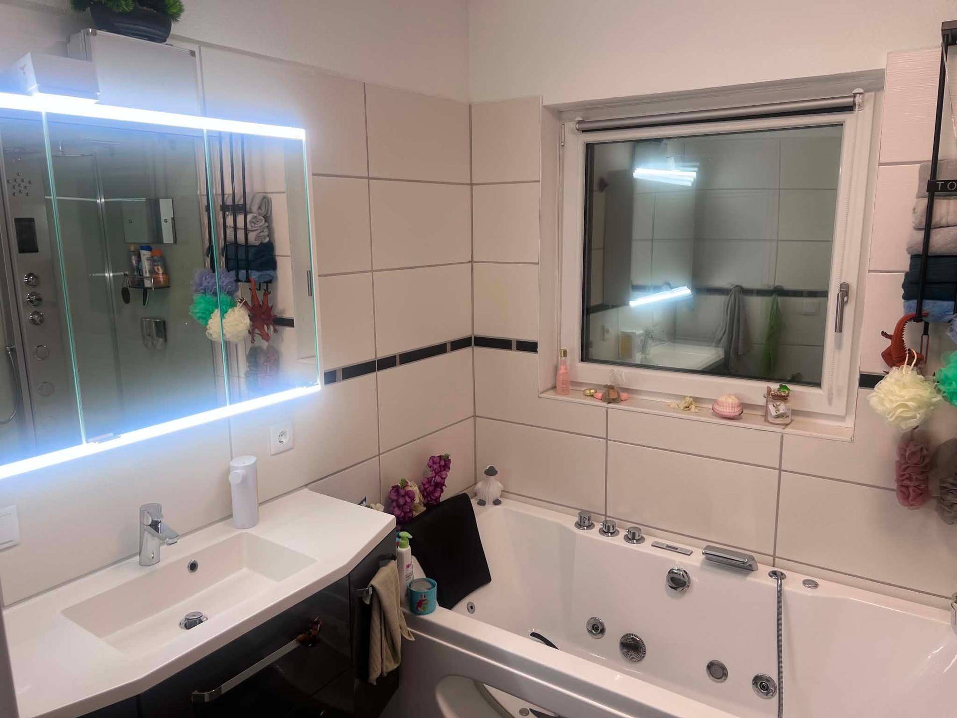 Modernes Badezimmer mit Whirlpool-Badewanne, Einzelwaschbecken und beleuchtetem Spiegelschrank.