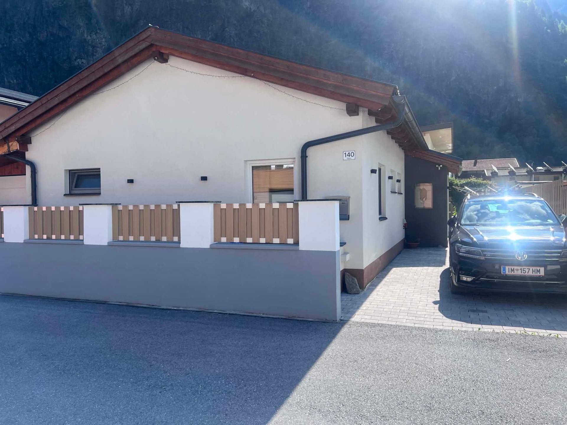 Ansicht des Hauses mit gepflasterter Einfahrt und einem geparkten Auto vor Bergkulisse.